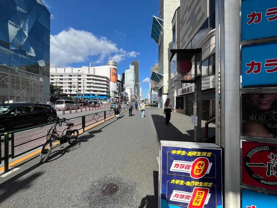 - 東京の繁華街の風景、青空の下、人々が行き交う商業エリア、店の看板と自転車が並ぶ歩道