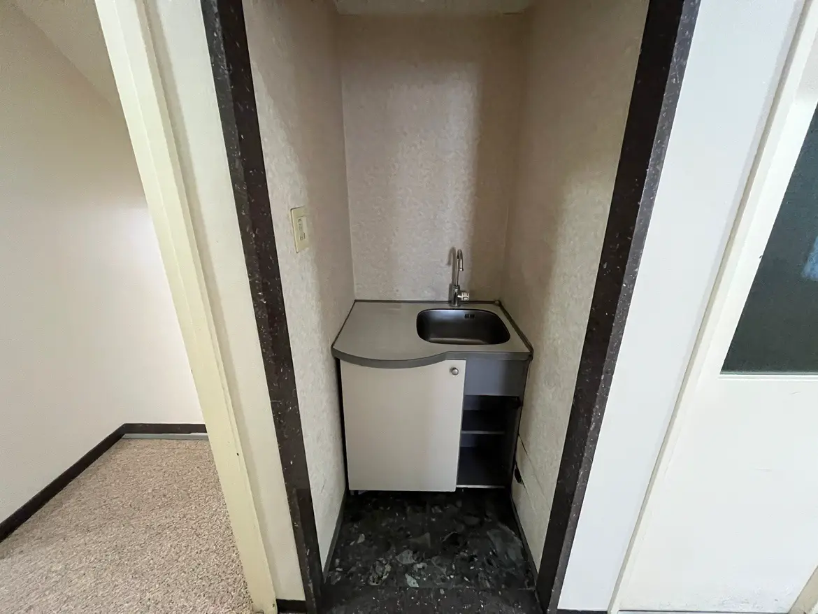 - 狭めのキッチンエリア、シンプルなシンクと収納が備えられたカウンター、淡い色調の壁面が特徴のインテリア