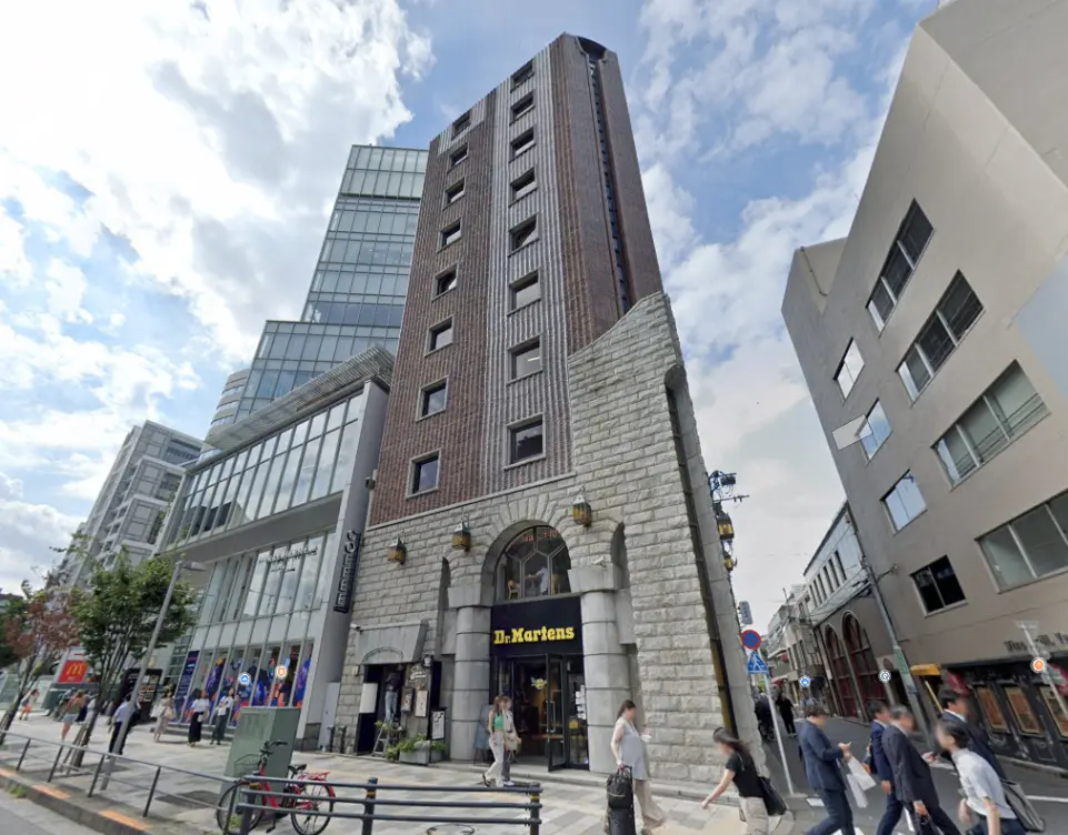 都会のビル街、歩道に多くの歩行者、地上階にドクターマーチンの店舗が入る商業ビル