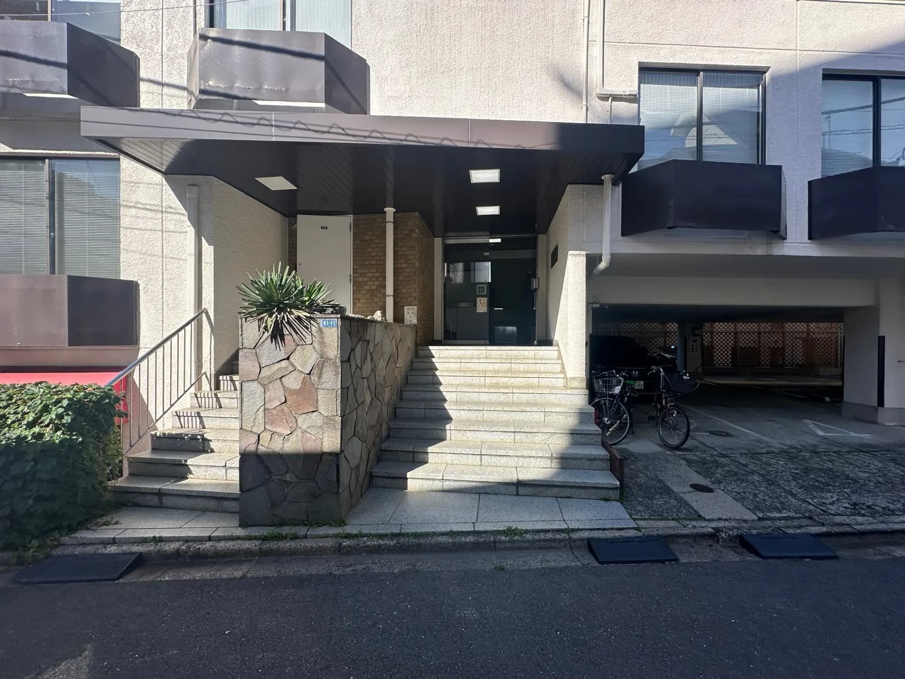 日々の生活シーンに溶け込む現代的なアパートのエントランス、石造りの階段と植栽、駐輪スペース付き