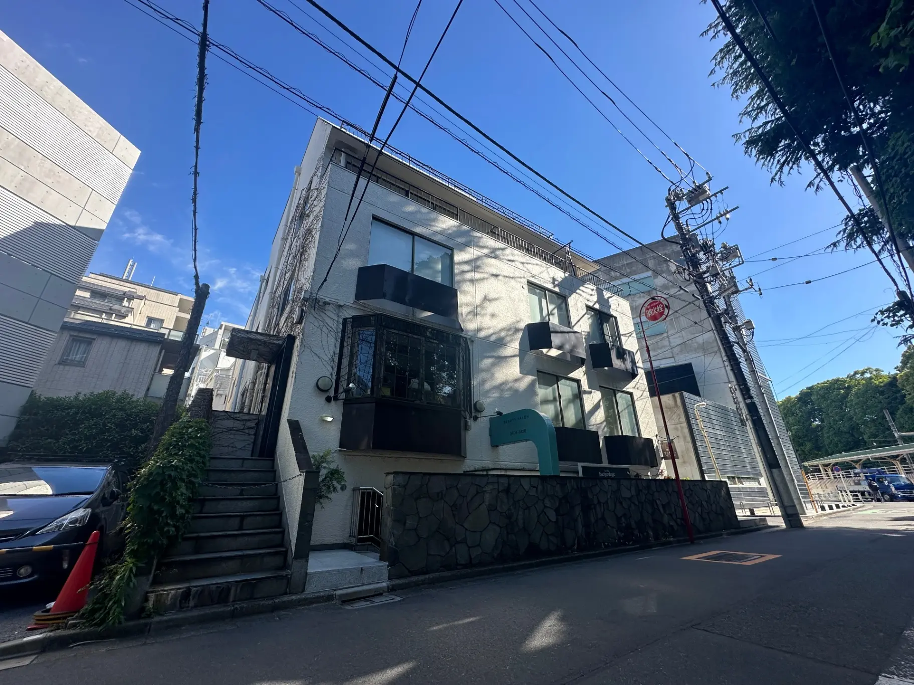 青空に囲まれた都市の景観、モダンな建築スタイルの建物、前面に階段と電信柱が見えるストリートビュー