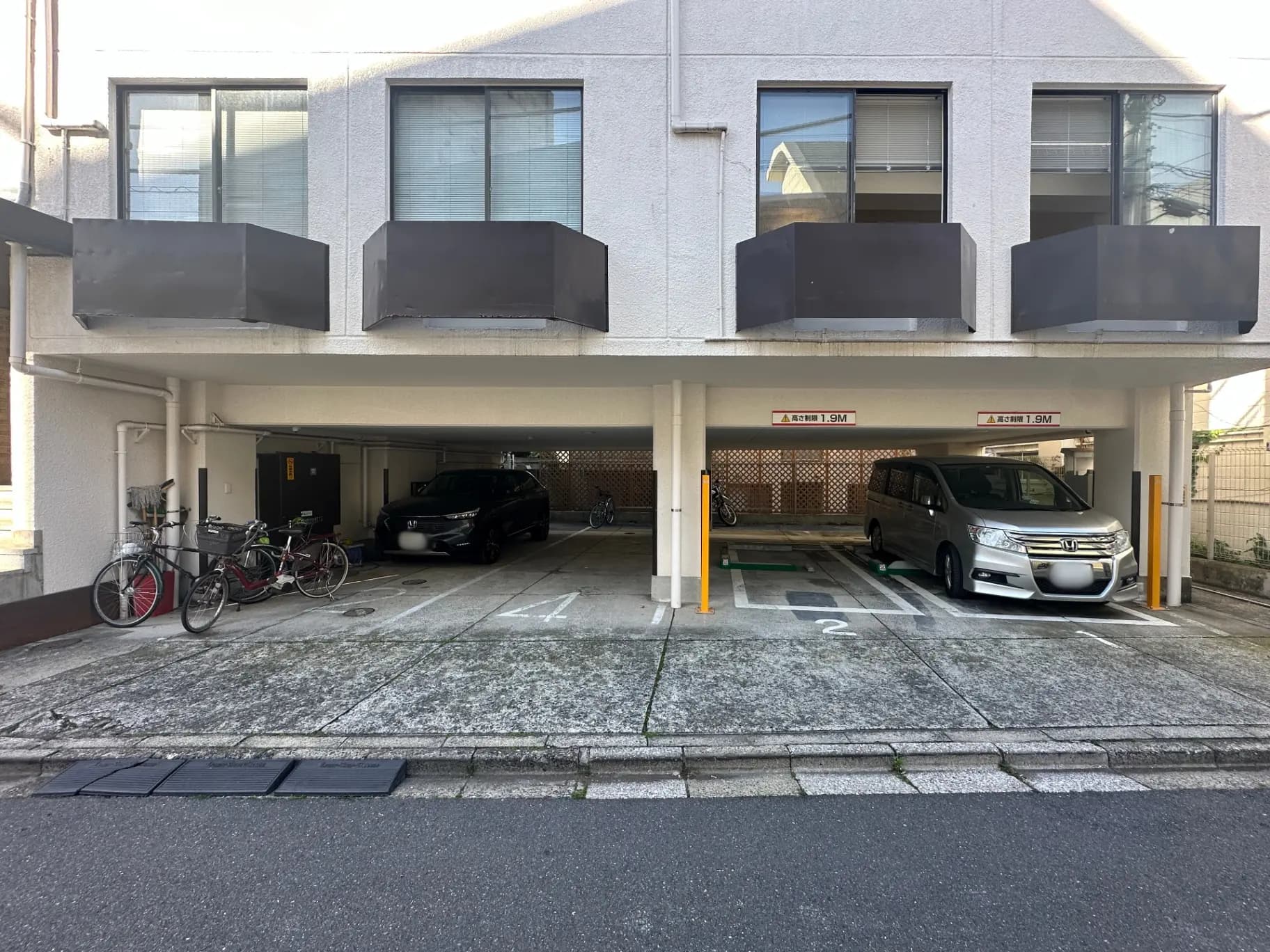 都市型マンションの屋外駐車場、自転車と車が停車中、バルコニーが特徴的な建物ファサード