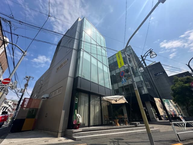 現代的な外観の都市型オフィスビル、ガラスと金属素材を使用したファサード、青空と電線が映るクリアな日中のシーン