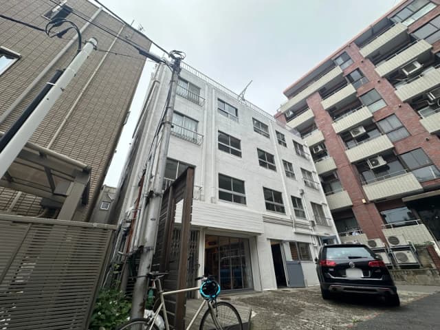 都市のアパート群、配管が見える外観、駐車中の車と自転車がある風景