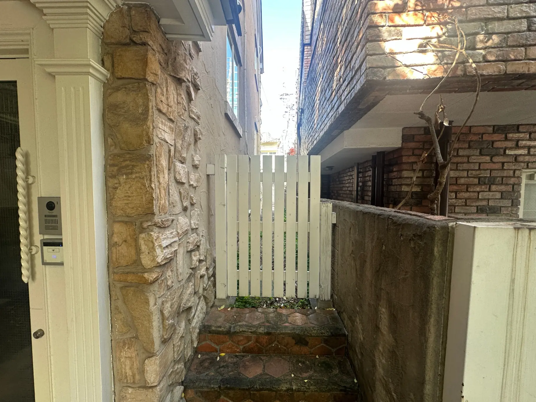 石造りの壁と白いフェンスがある門の入り口、インターホン付きの家の外観