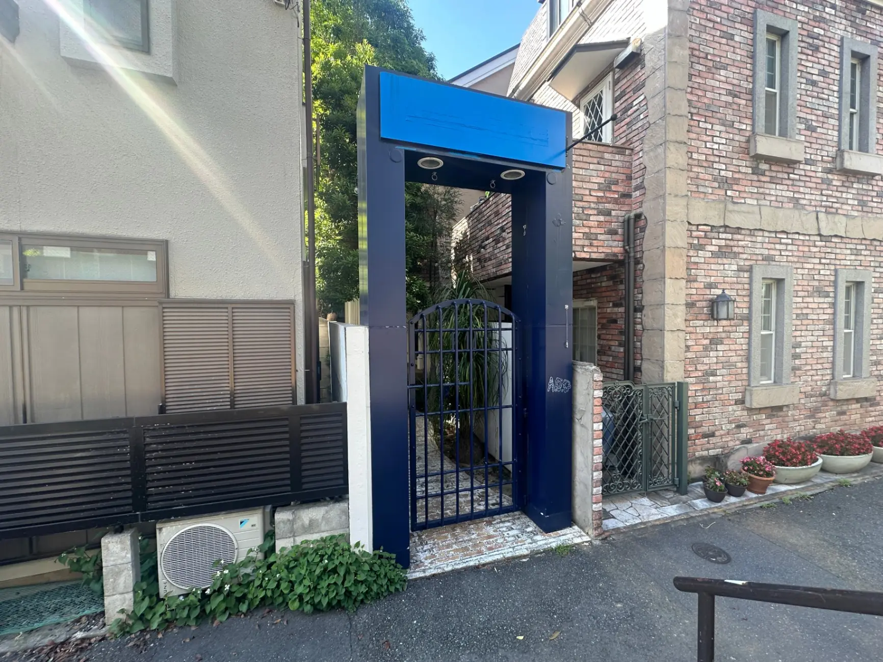 青い門柱とレンガ造りの外壁、植木鉢のある家の玄関エントリー