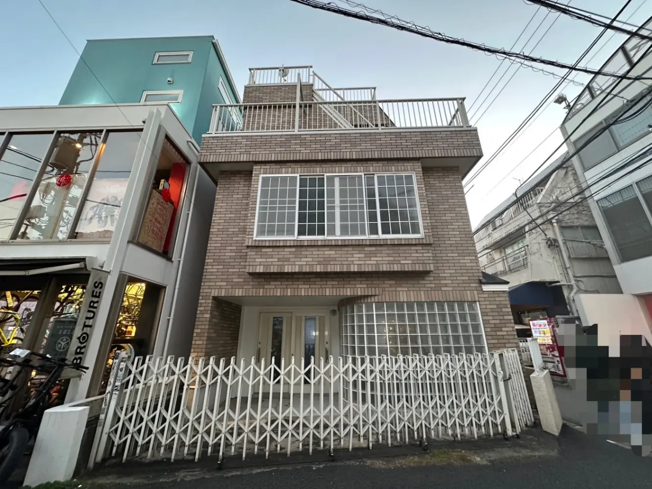 都市の住宅街にあるモダンな三階建ての建物、白いフェンスとレンガ調の外壁