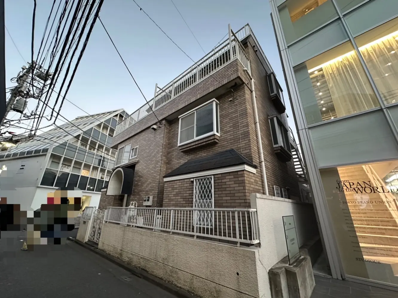 都市の住宅街にあるレンガ造りのアパート風建物、隣接するモダンなガラス張りの建築物、電線と明るい空