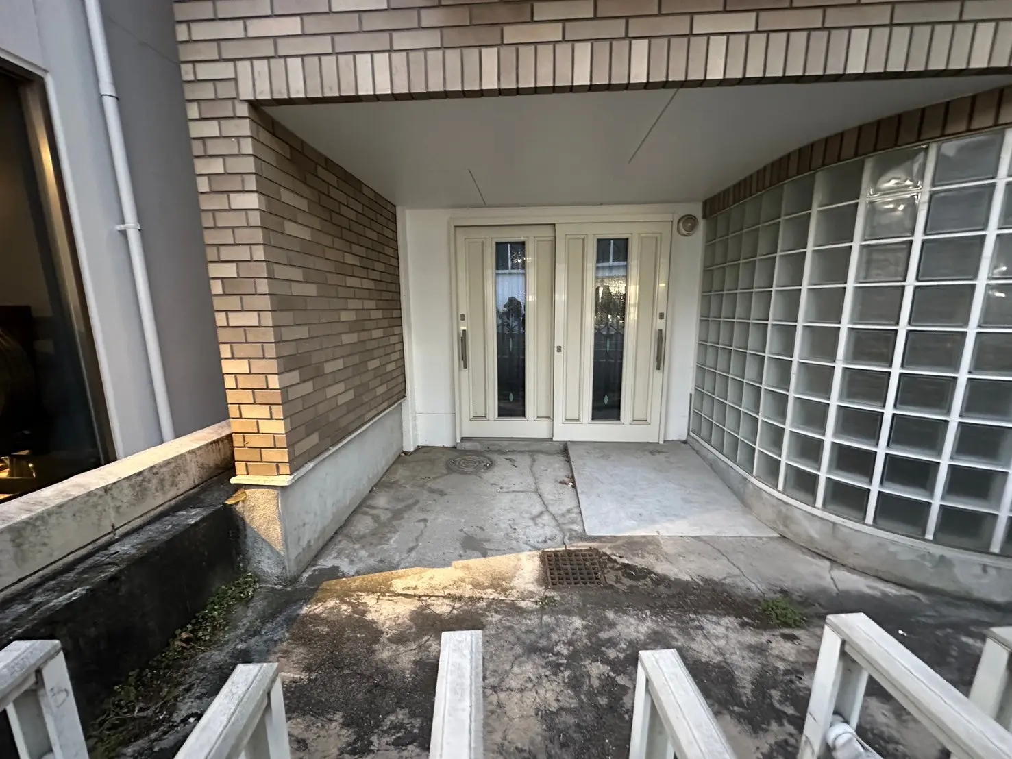 レンガ造りのエントランスにガラスブロックの壁、白いドアのある住宅外観