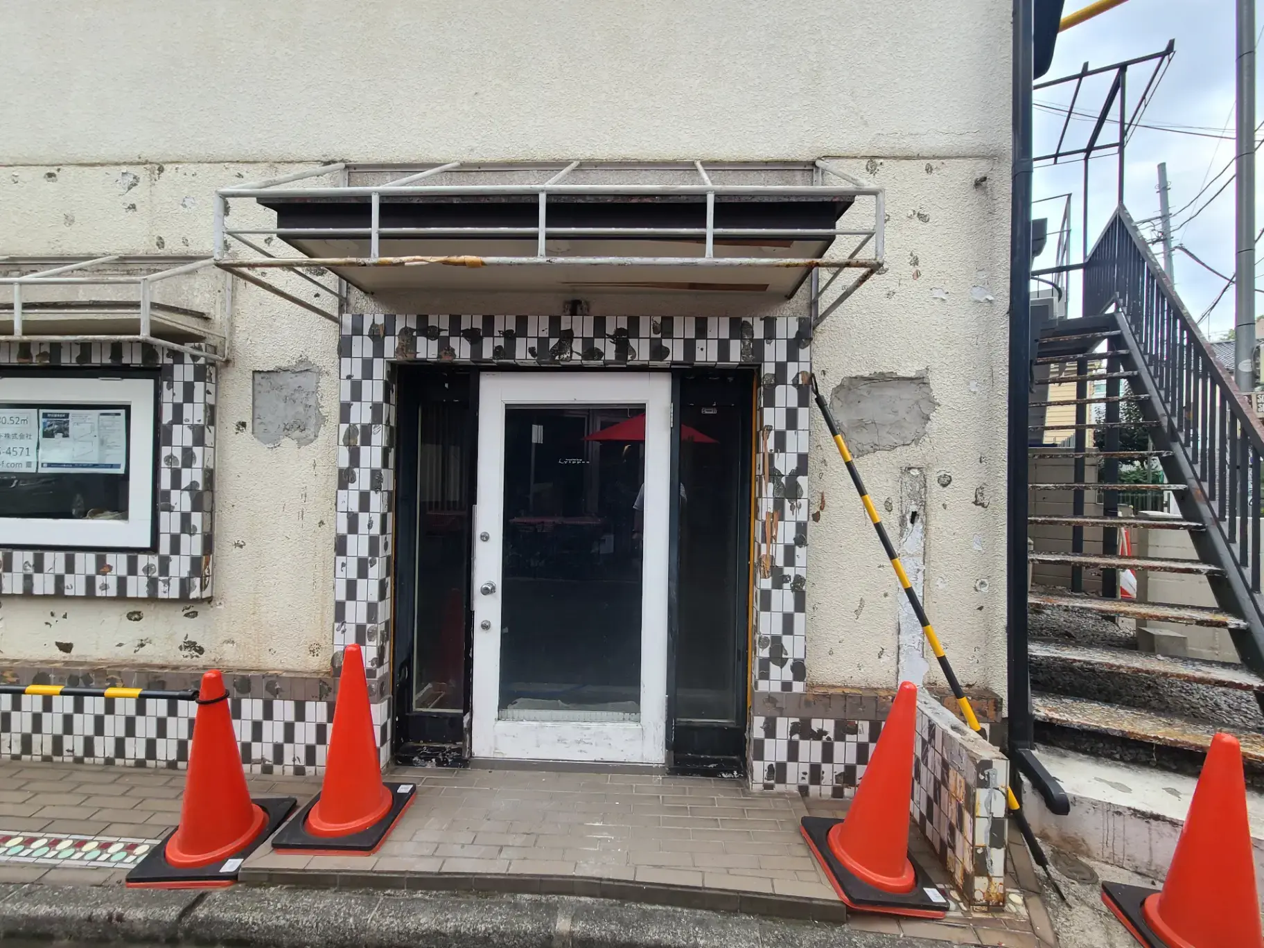 "都市の建物の入口に配された赤い交通コーンと段差注意の黄色いライン"