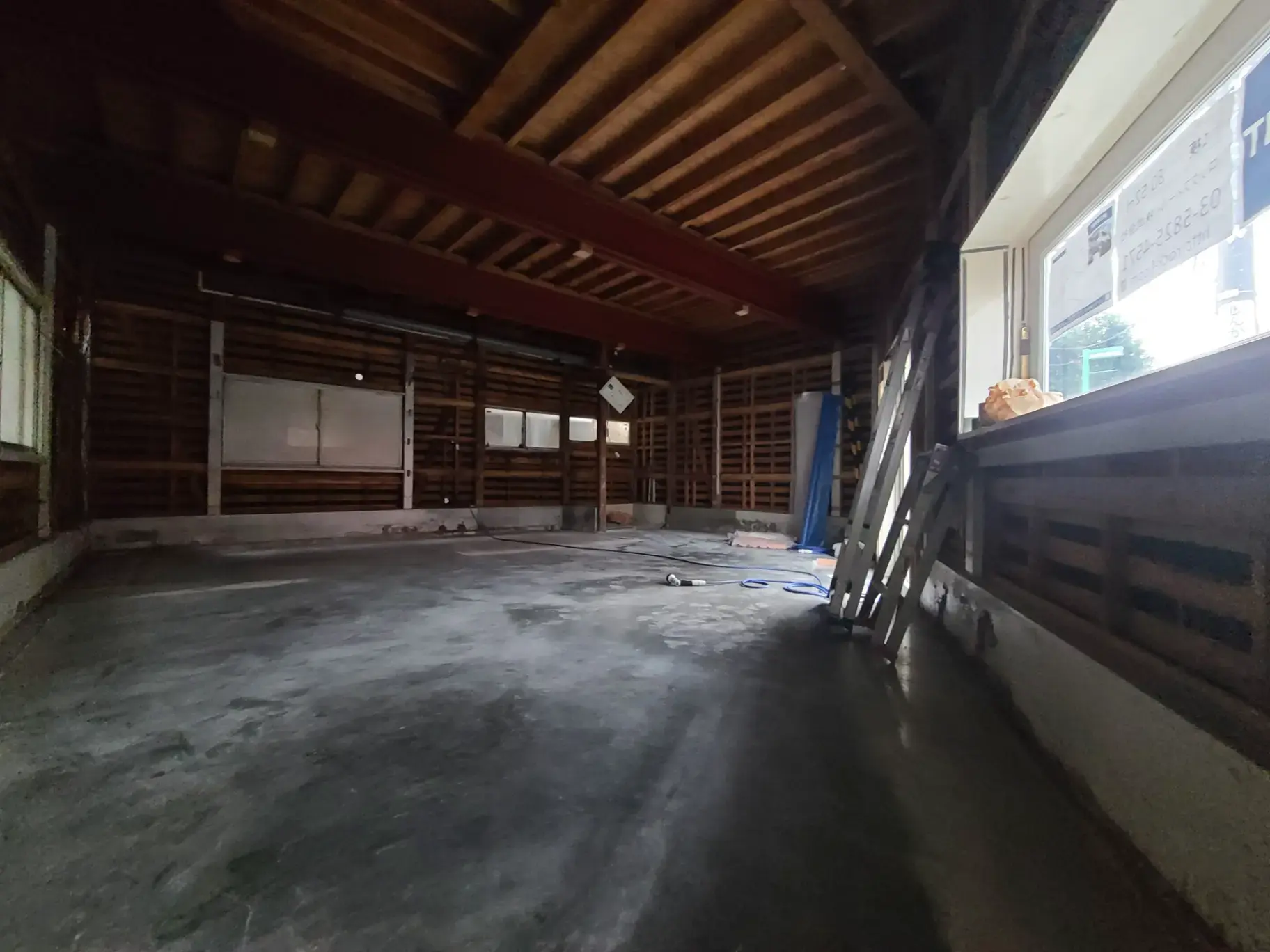 「広々とした空のガレージ内部の写真、コンクリートの床と木製の梁が見える」