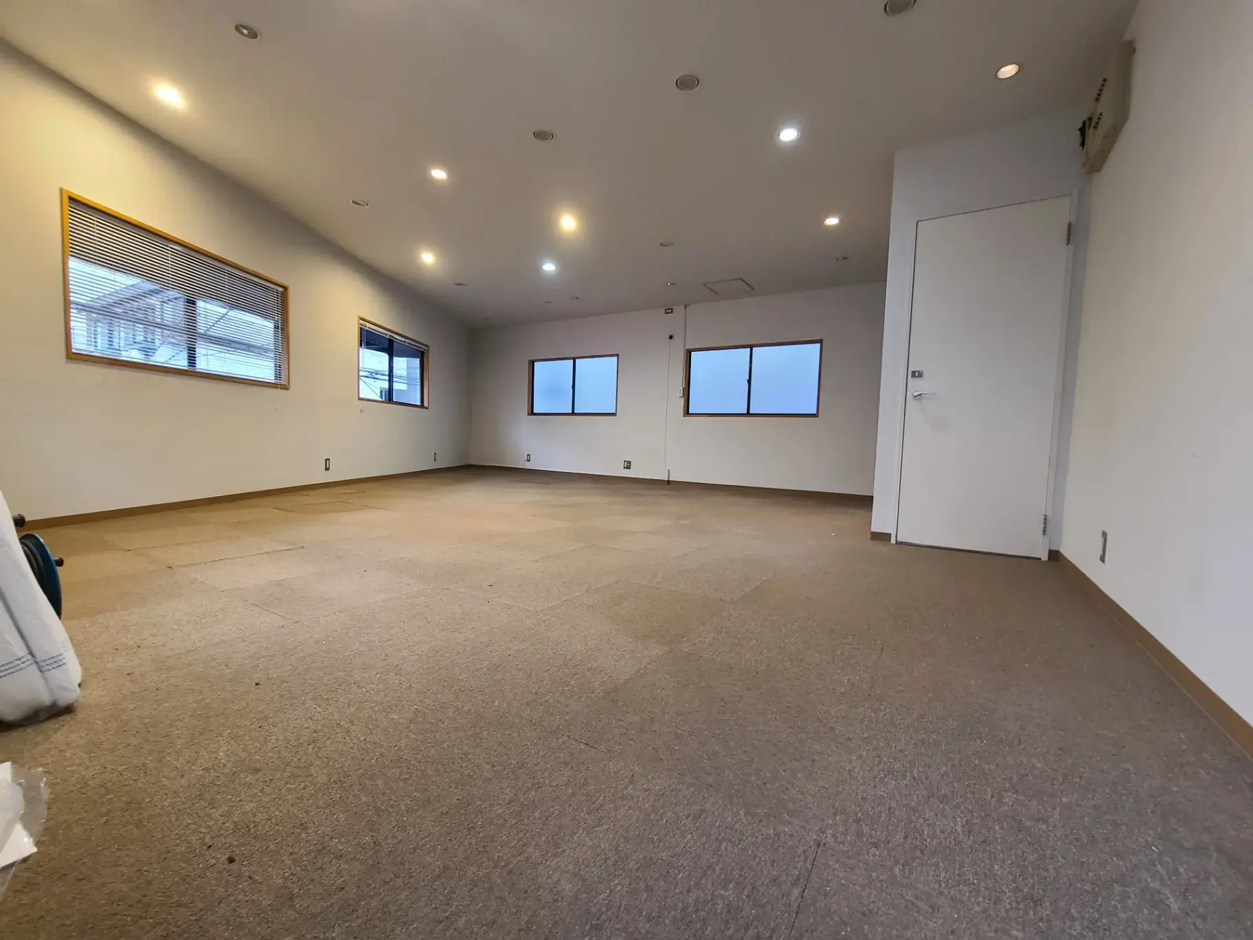 空のオフィス室内、白い壁とカーペット、天井のダウンライト、窓のある明るい部屋