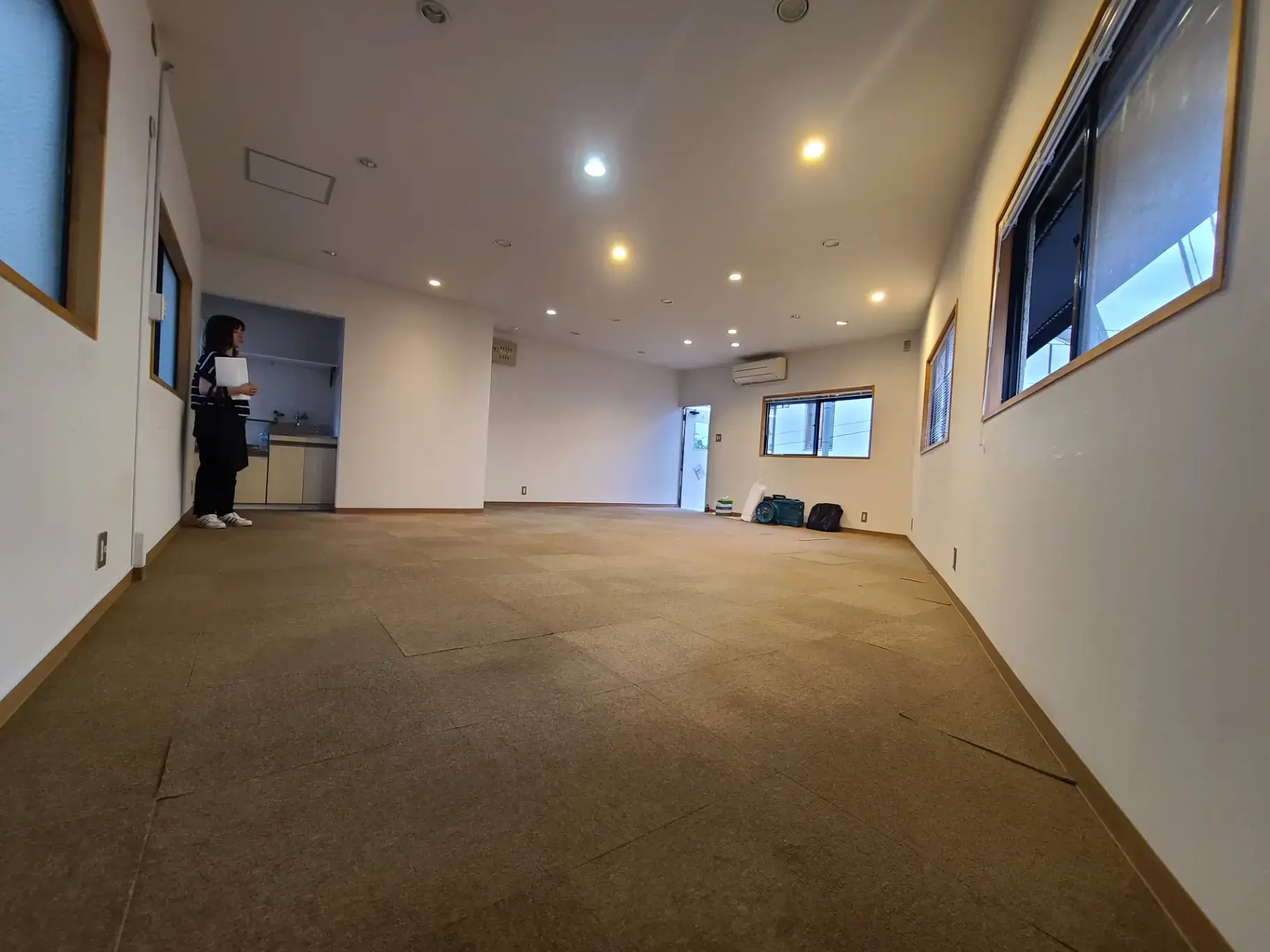 画像のAlt属性を以下のように設定することをお勧めします:
"広々とした明るいオフィススペースに立つ人物、窓と照明が付いた室内の様子"