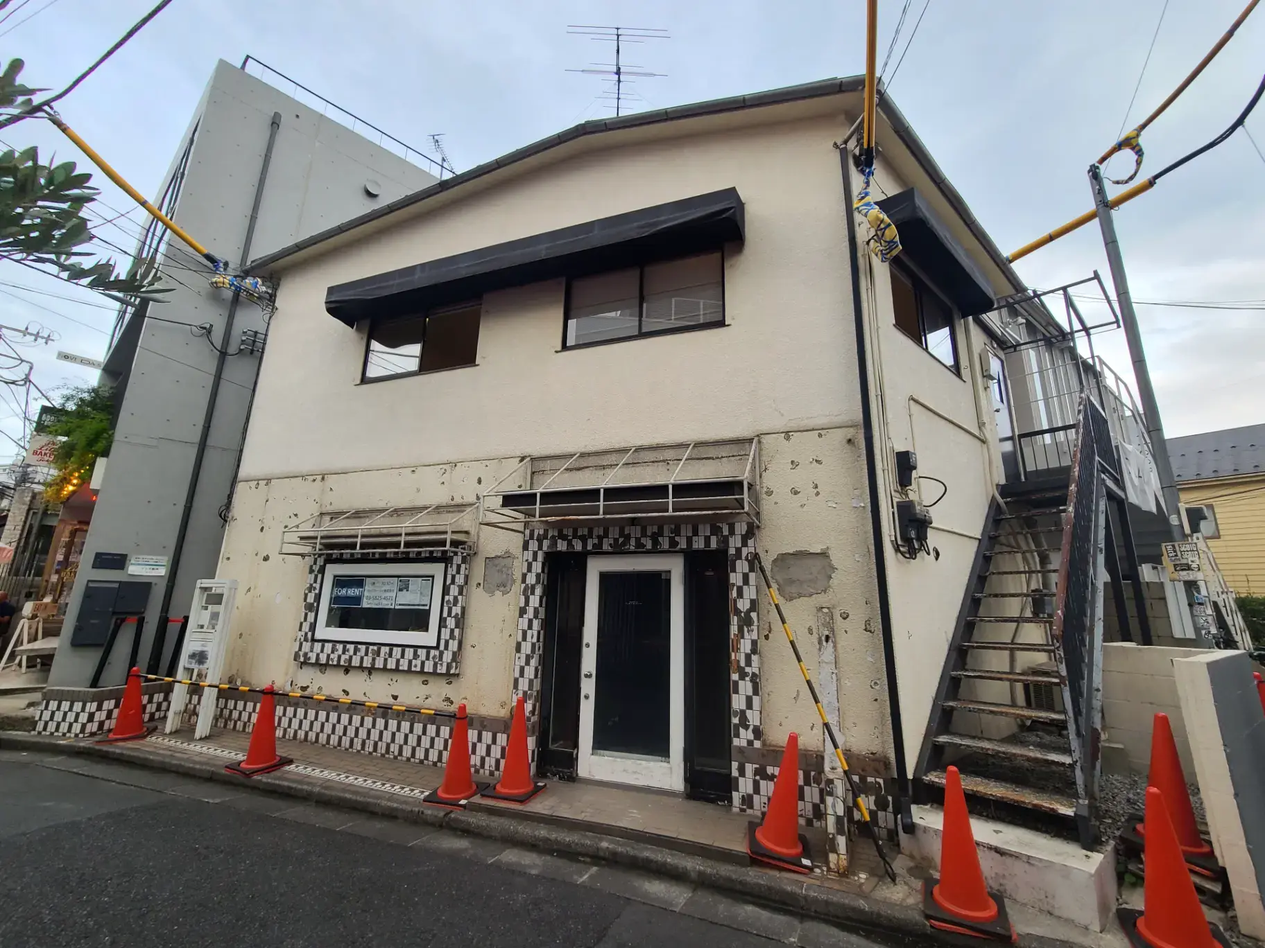 "日本の都市部にある古くからの建物の外観と修理作業用のオレンジの交通コーン"