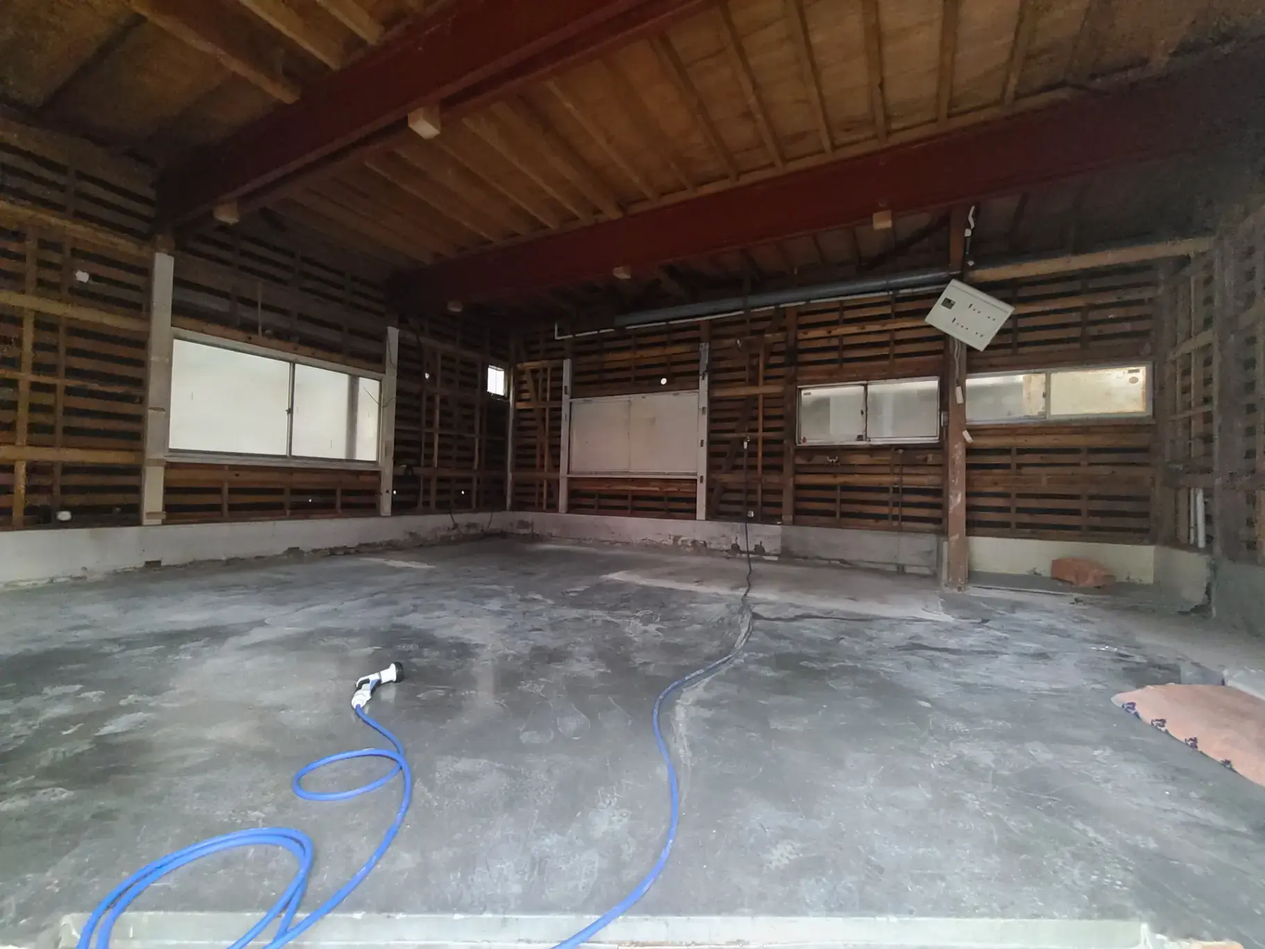 「改装前の古い倉庫内部の空間、コンクリートの床と木製格子の壁」