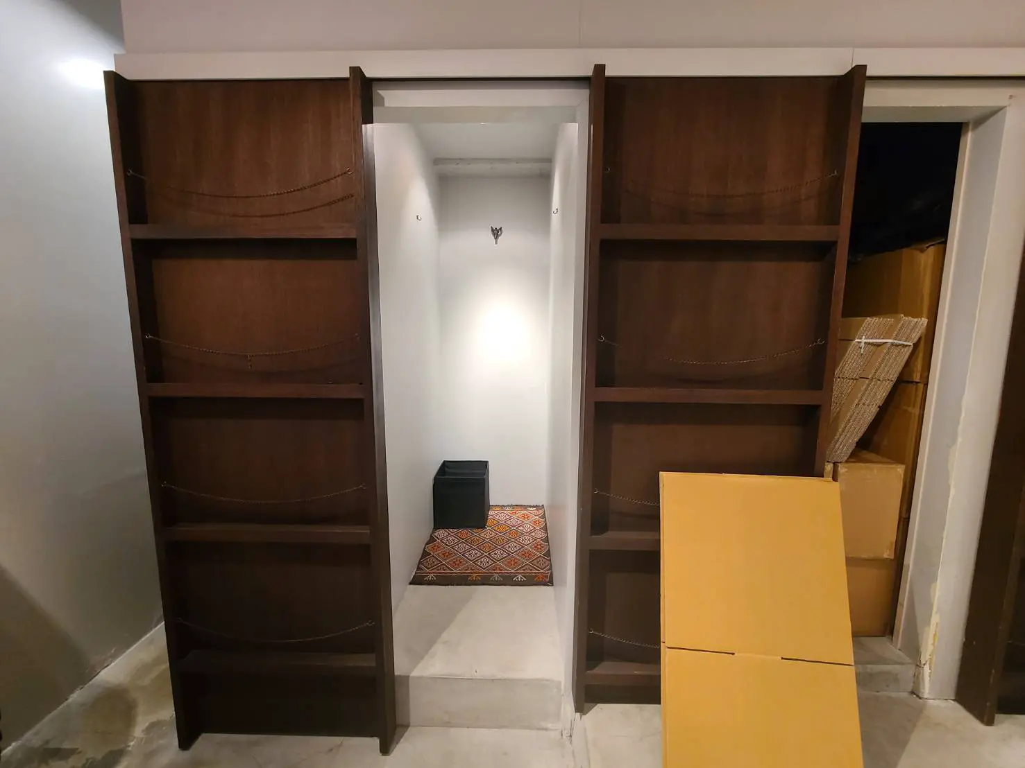 改装前の部屋、空の棚と中央の黒いスツール、左側に置かれた段ボール箱