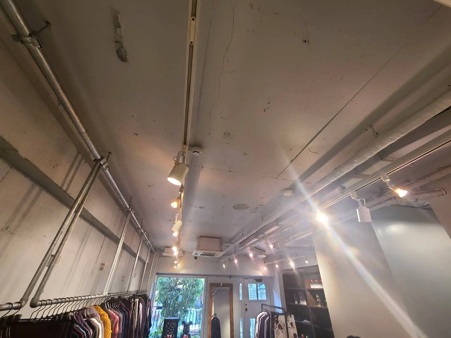 工業的なデザインのアパレルショップ内部、露出した配管と照明、掛けられた服