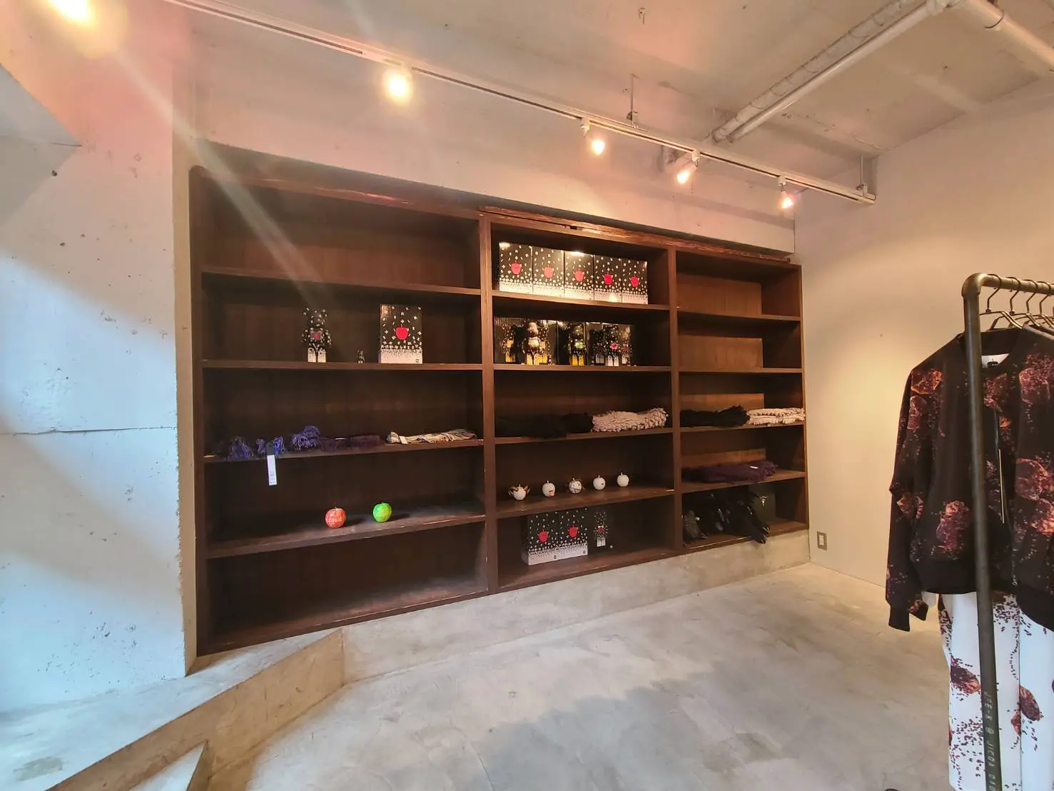 シンプルなデザインの洋服店内部、木製の大きなシェルフとハンガーラックに陳列された商品