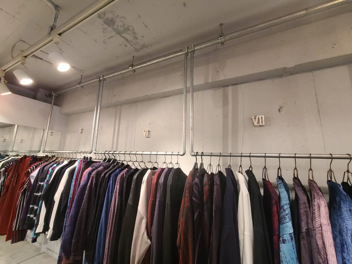 シンプルなデザインの服が並ぶセレクトショップ内部、コンクリートの壁とインダストリアルな配管
