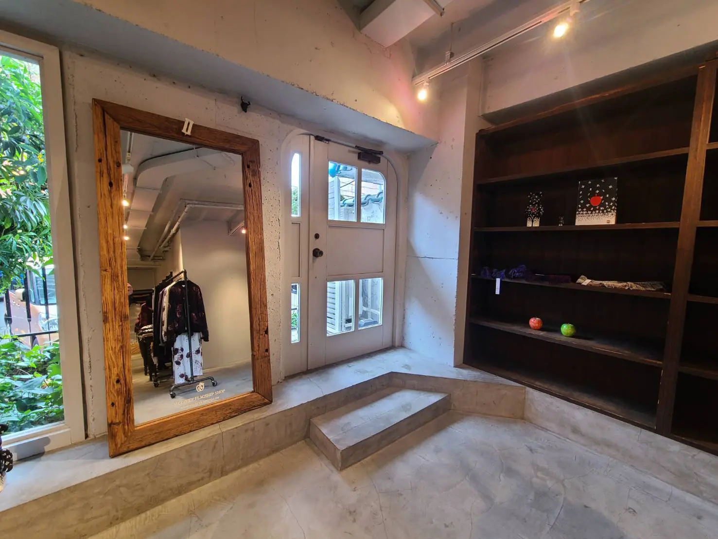 モダンな店内の一角、大きな木枠の鏡と陳列棚、コンクリートの壁、天井からのスポットライティング