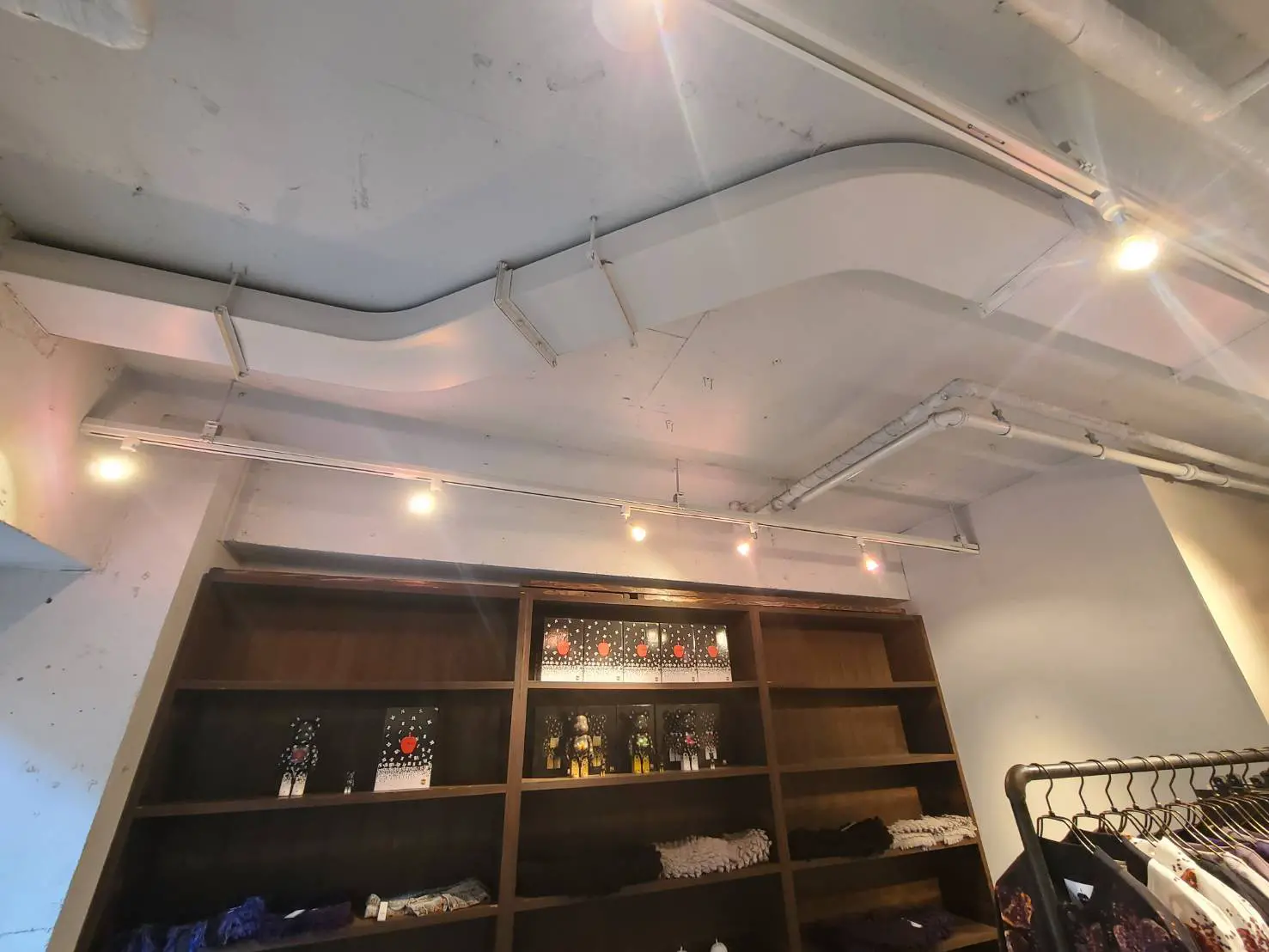 インダストリアルデザインのファッションショップ内部、ダクトが露出した天井と木製の棚、照明が設置されたおしゃれな空間