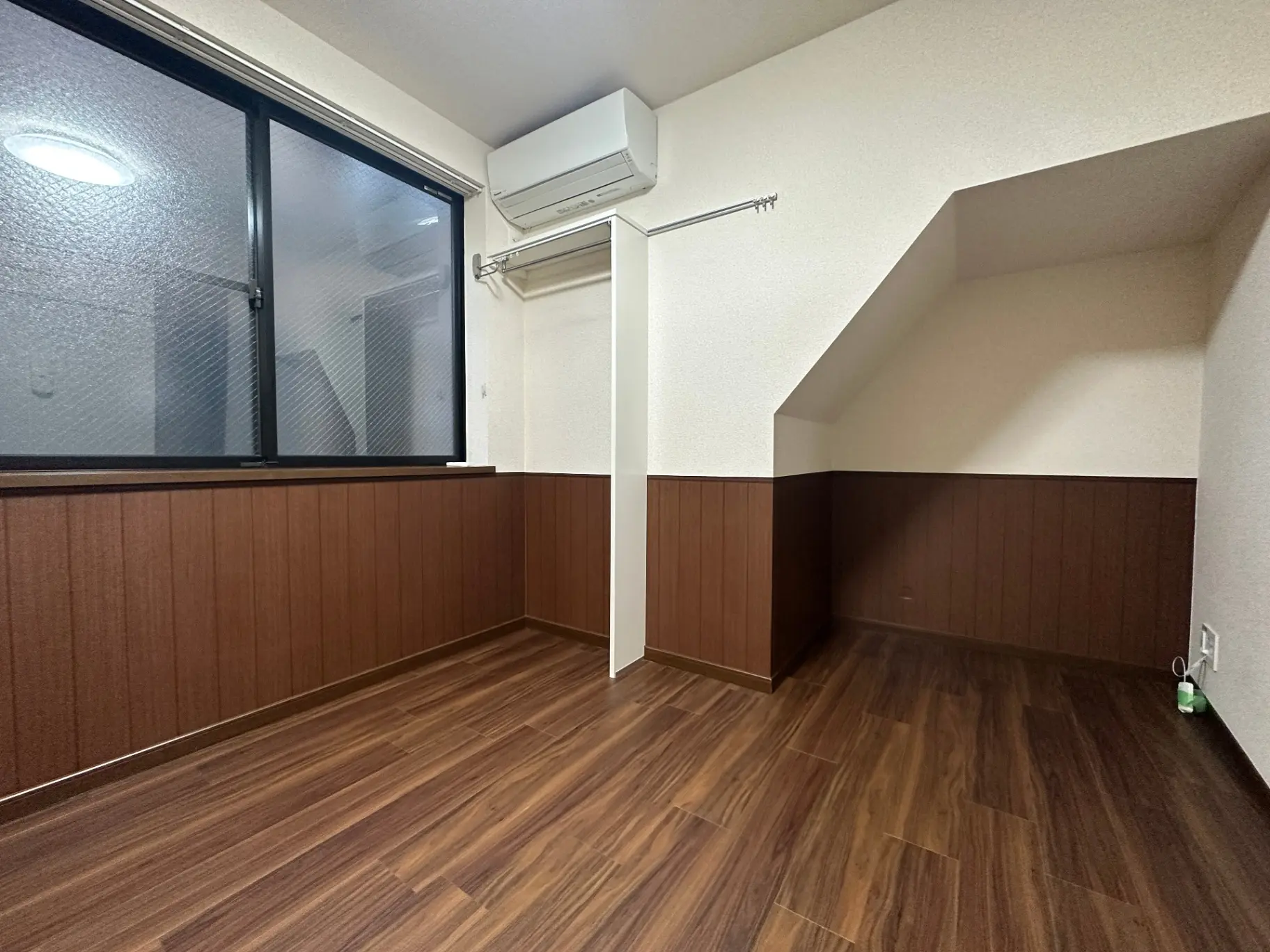 エアコン付きの落ち着いた色調の居室、広い窓と木目調のフローリング