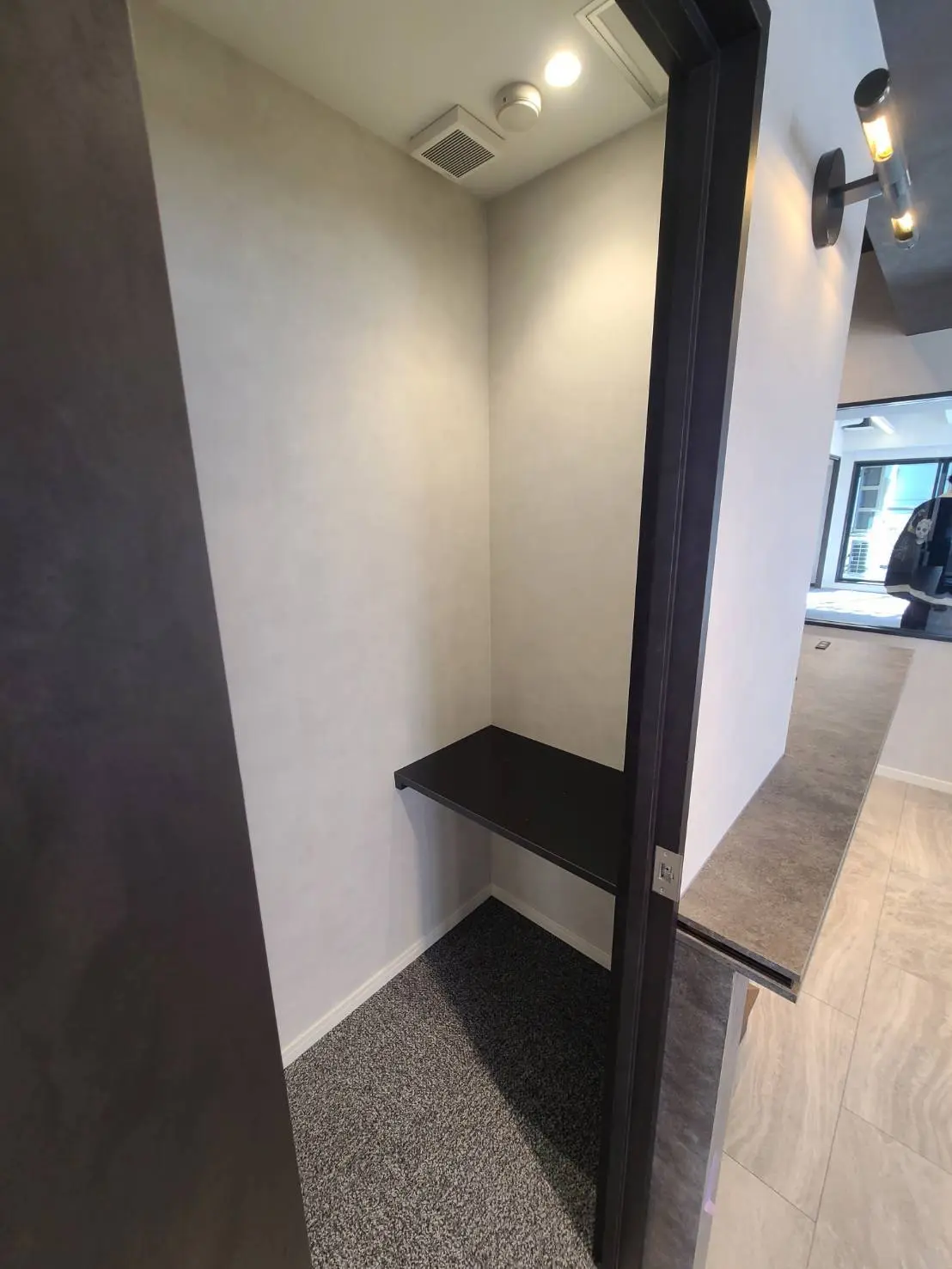 シンプルなデザインの玄関ホール、グレーのカーペットとブラックの棚が特徴的なモダンなインテリア