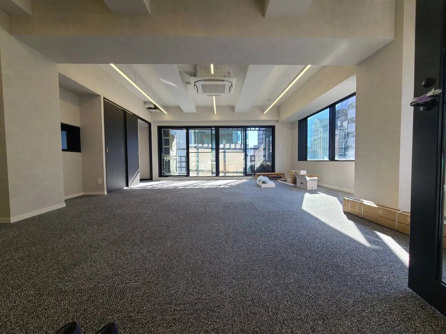 広々としたオフィス空間、カーペット敷きのフロア、自然光が差し込む大きな窓とモダンな照明設備