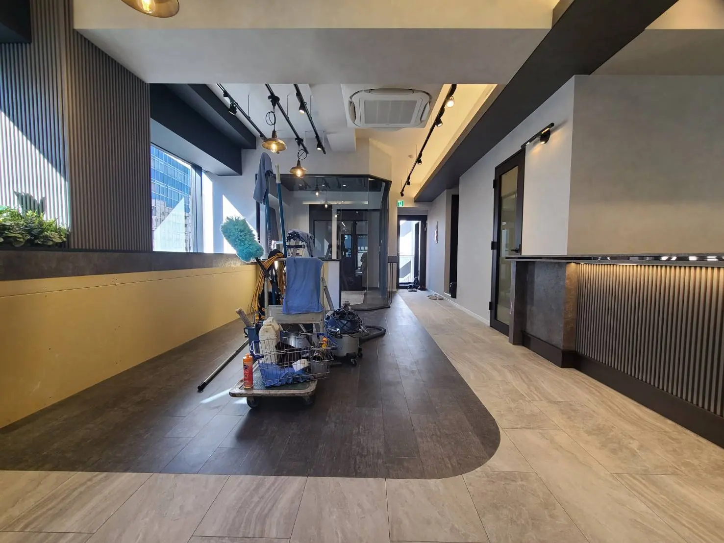 ビルのロビー内部、清掃機器が置かれた通路、モダンなインテリアデザインと窓からの自然光