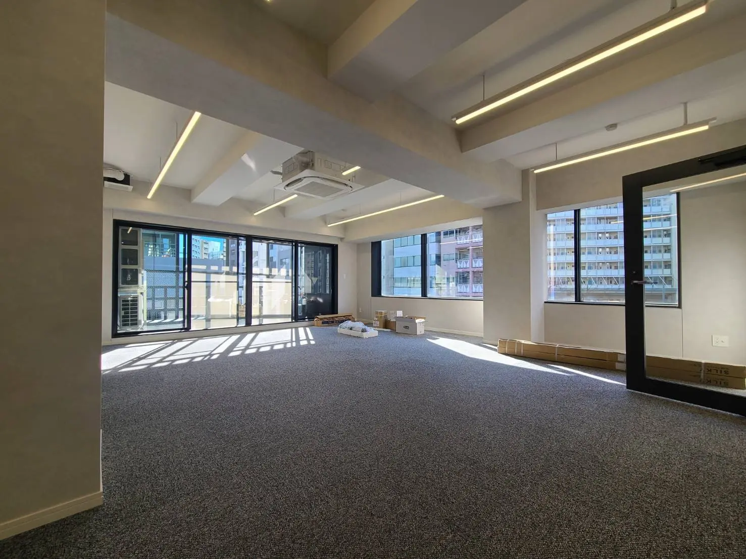 空間が広く明るいオフィスのインテリア、天井のモダンな照明、大きな窓から見える都市の景色