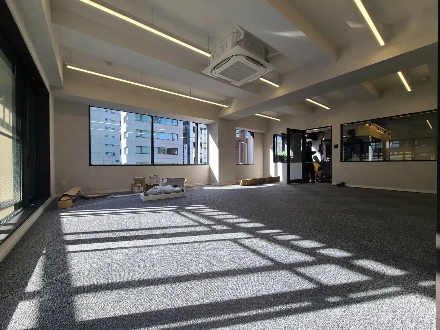 空間に余裕がある現代的なオフィス、天井にはオシャレな照明、広い窓から差し込む自然光