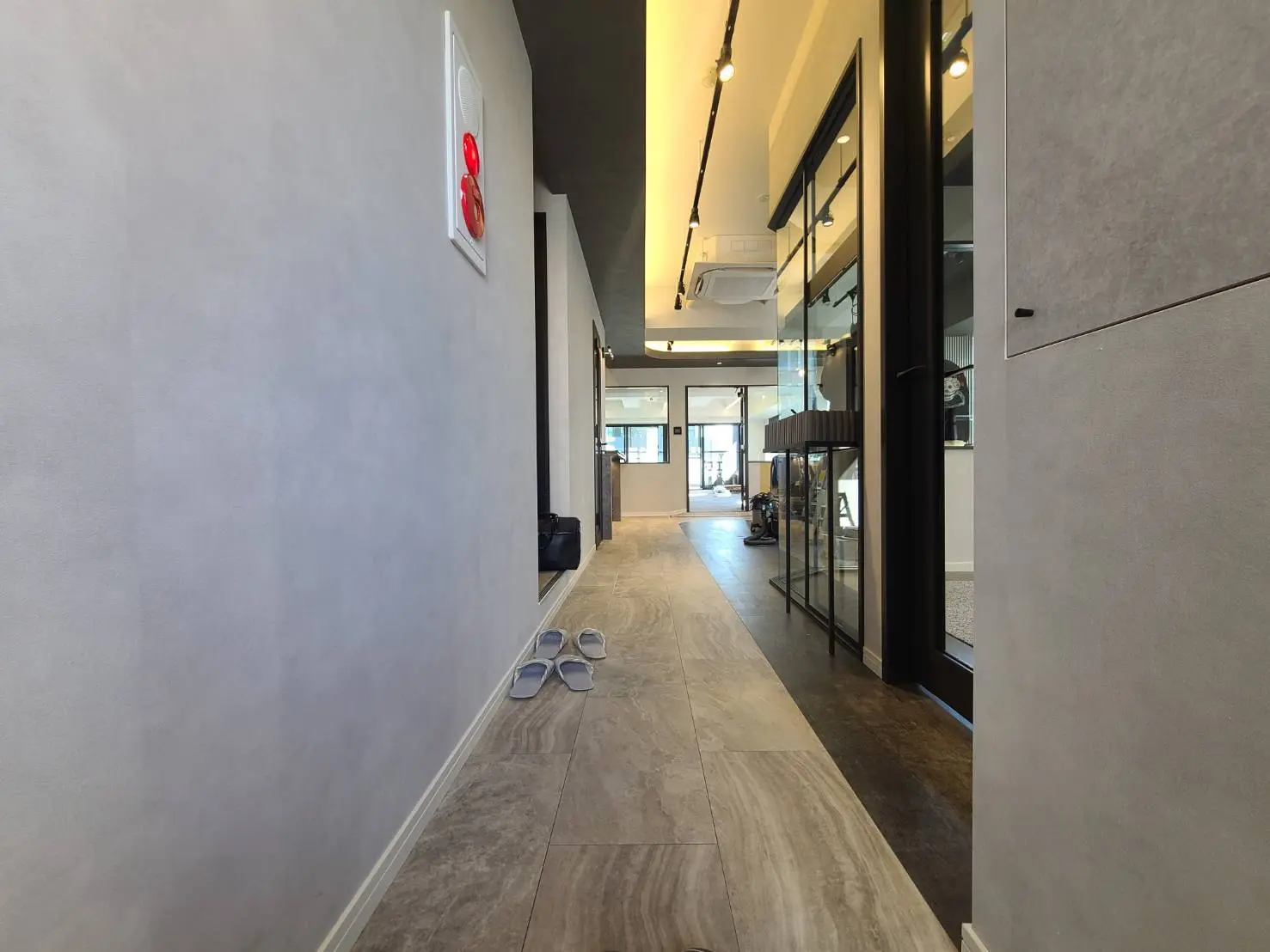 モダンスタイルの廊下、グレーの壁とタイルフローリング、天井にはスポットライトがあり、木製の靴箱とガラスドアが見えるインテリア