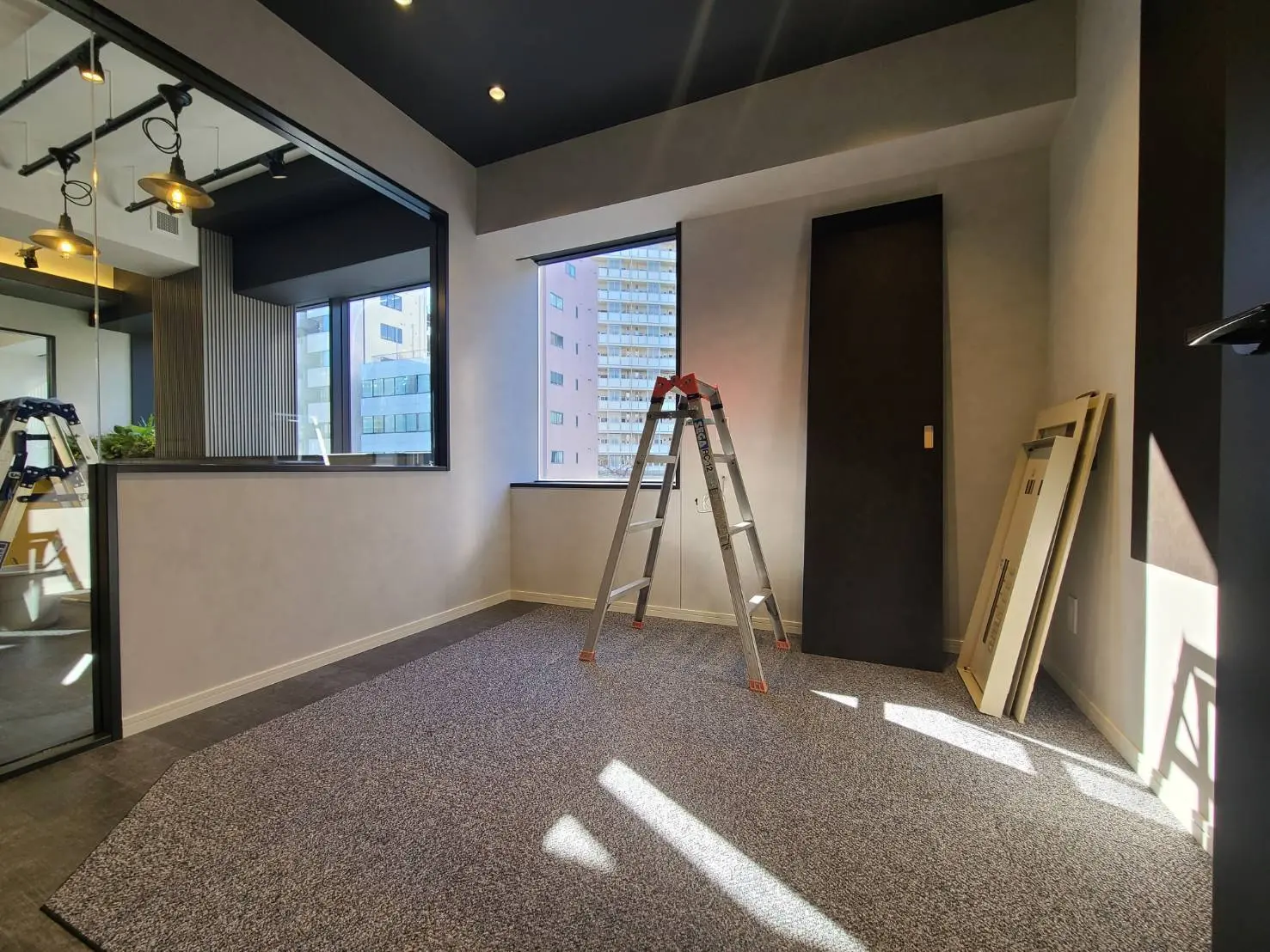 リノベーション中のモダンなオフィススペース、工事用のはしごと資材が置かれた部屋、大きな窓からの自然光