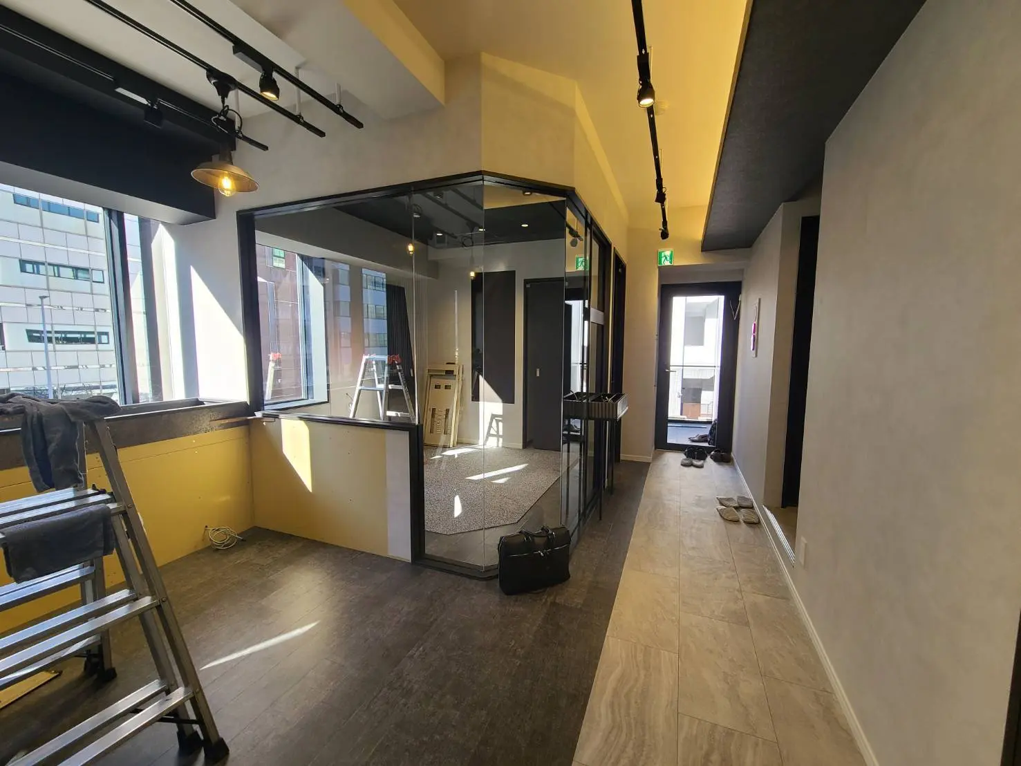改装途中のオフィス空間、天井にトラックライト、ガラスのパーティション、大きな窓からの自然光