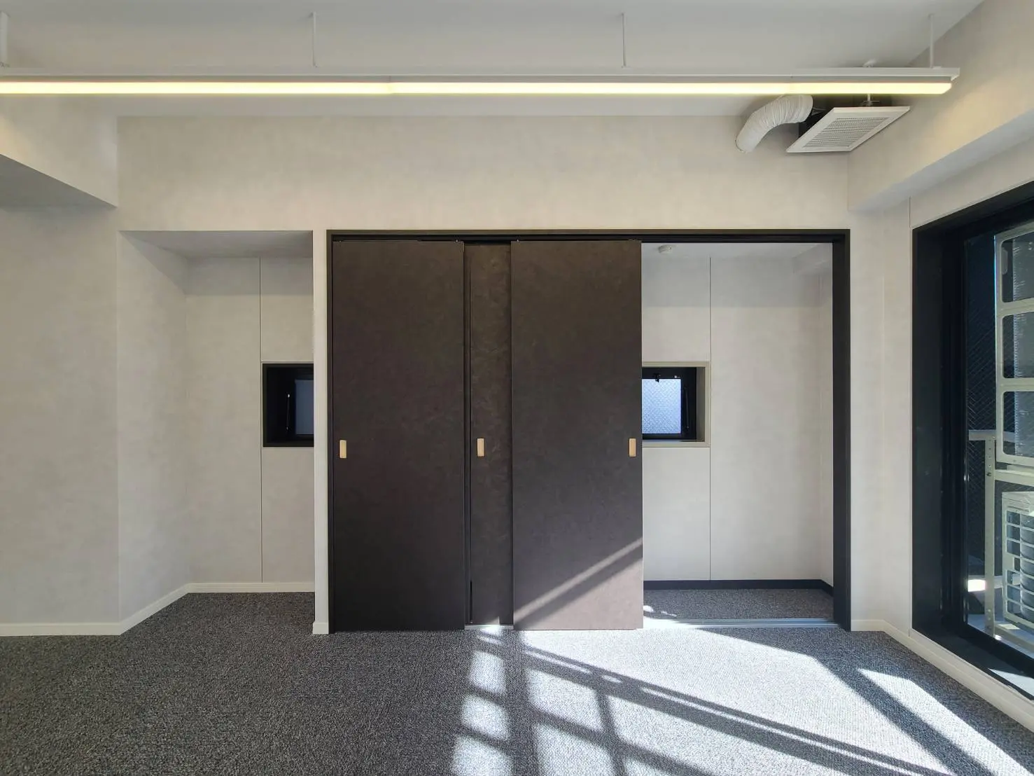 シンプルなデザインの玄関部分、ダークブラウンのドア、サイドに小窓、天井には長方形の照明