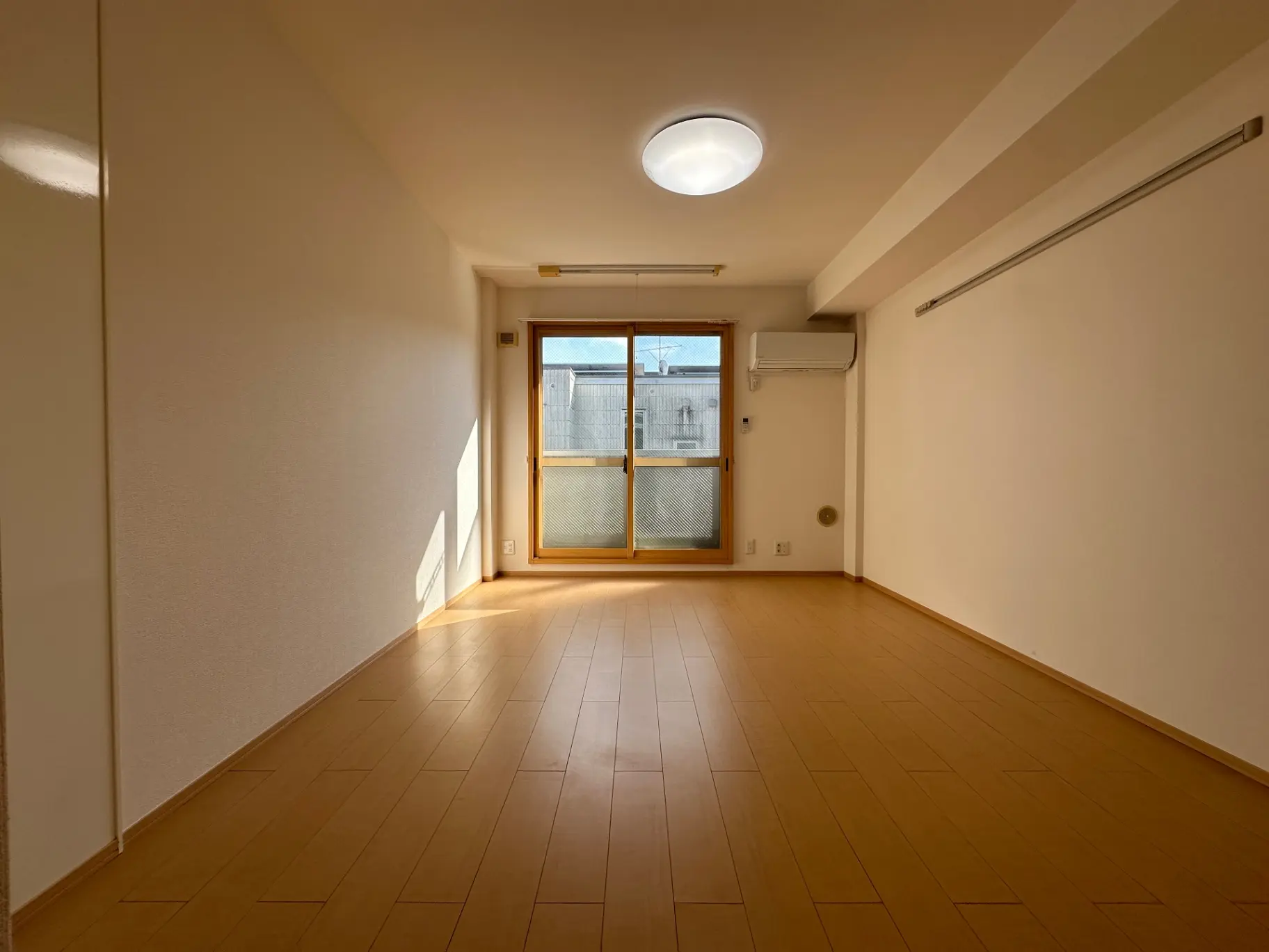 明るい日差しが入る空の部屋、清潔感のあるベージュ色の壁、床暖房付きの木目調フローリング