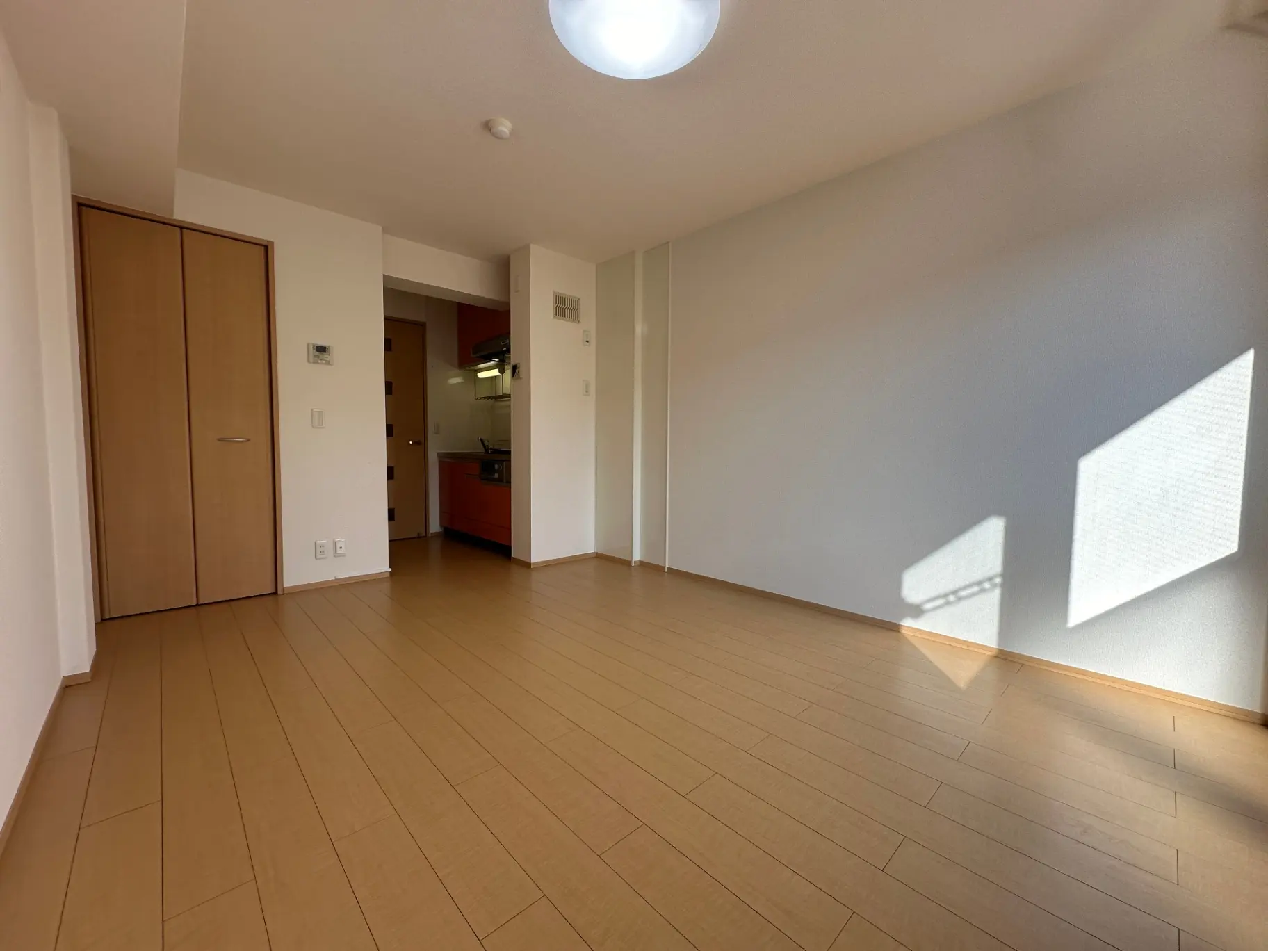 明るい日差しが差し込む広々とした空間、木目調のフローリングと白い壁のシンプルなリビングルーム