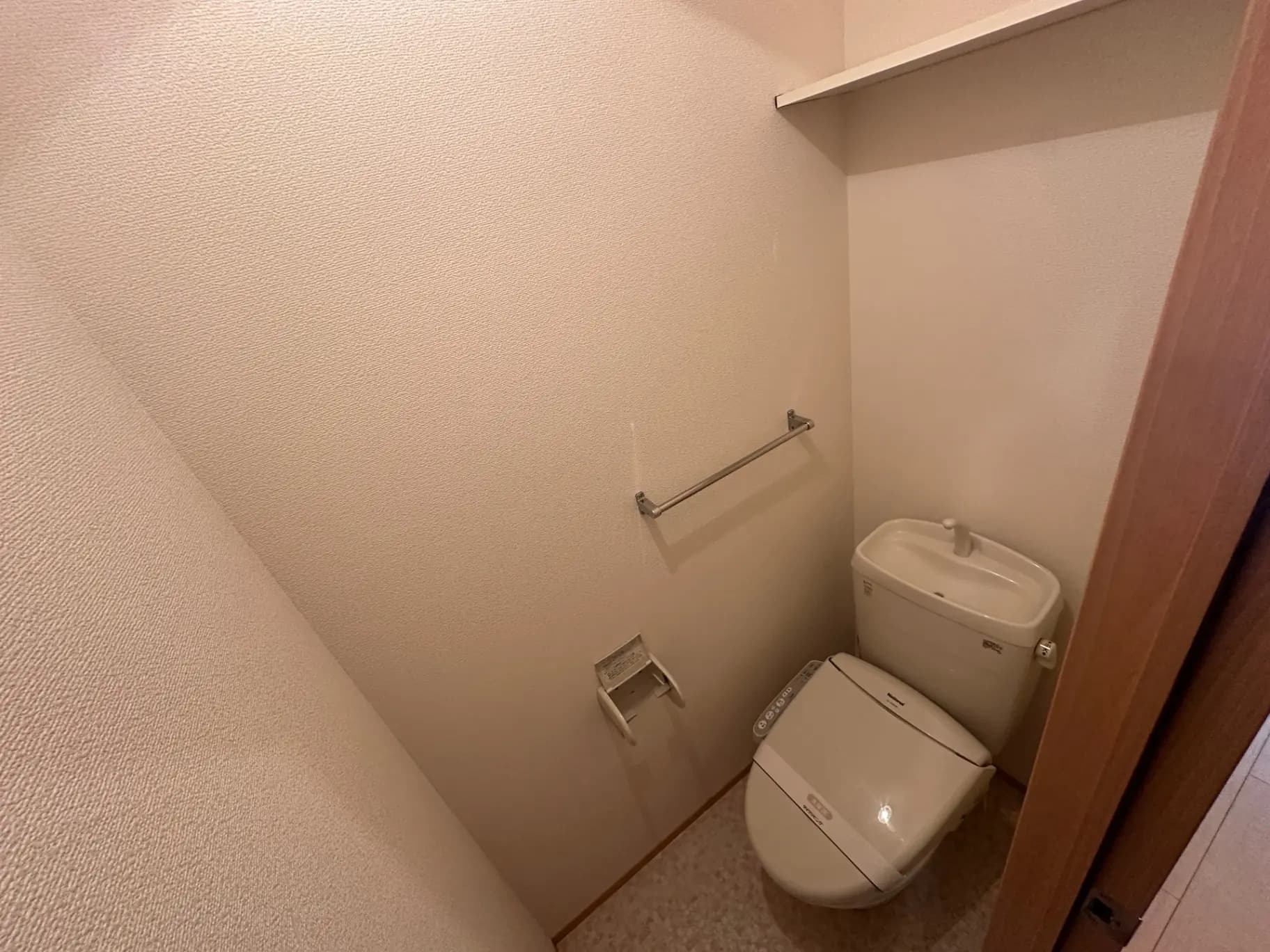 シンプルで清潔なトイレルーム、ホワイトの便器と手洗い付き、タオルホルダーとトイレットペーパーホルダーが壁に取り付けられている