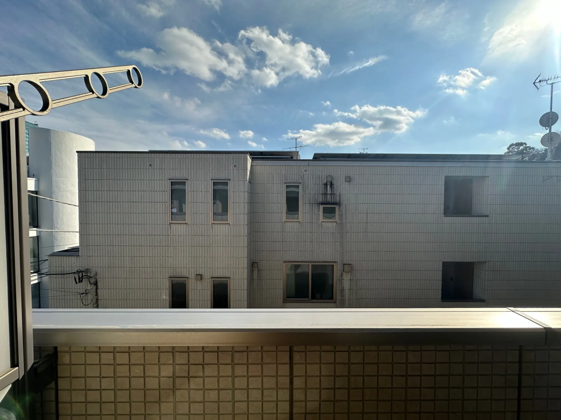 都市風景のマンションの外観、清潔感のあるホワイト壁面、日差しが差し込む窓とベランダ