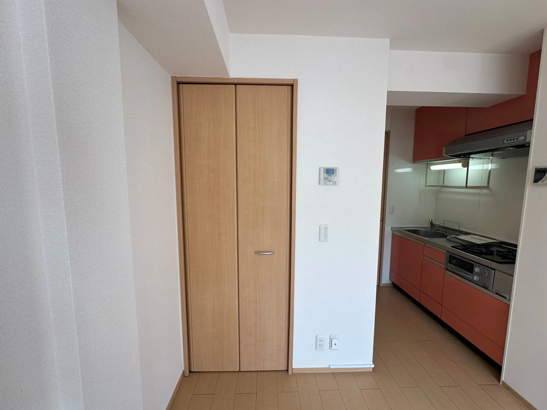 現代的なデザインのキッチン、木目調の扉とフローリング、オレンジ色のキャビネットとシルバーの家電が映えるインテリア