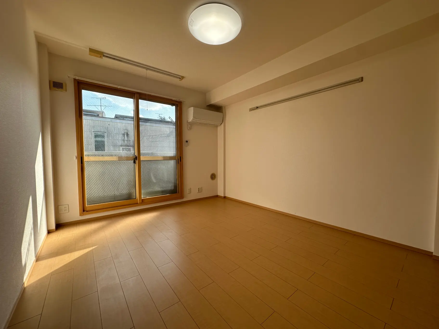 明るい日差しが差し込む木目調のフローリング、広々とした空間のリビングルーム