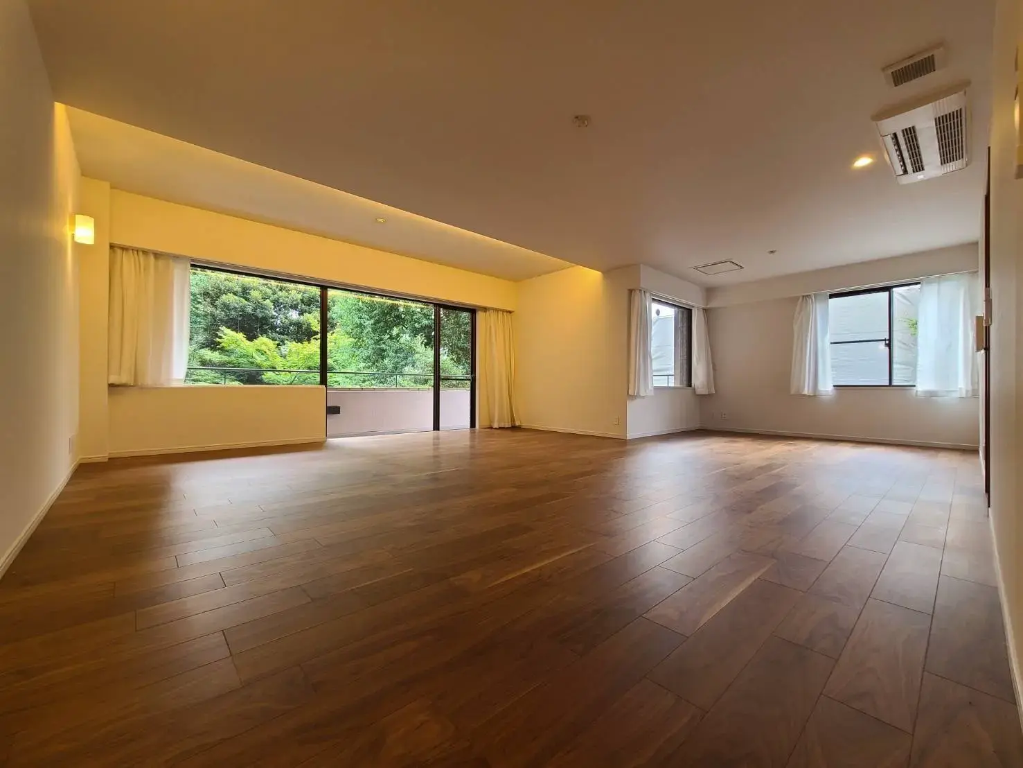 広々とした明るいリビングルーム、木製フローリング、大きな窓から見える緑豊かな景色