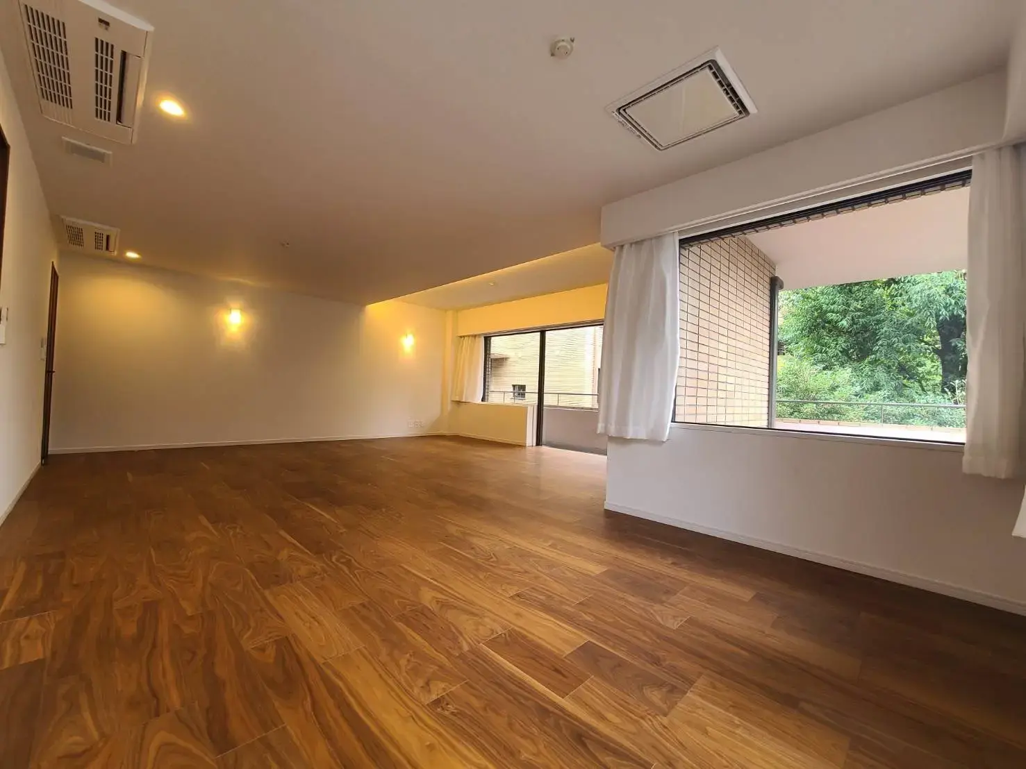 空間が広々とした明るいリビングルームで窓から自然光が入る木目調フローリングのアパート内装