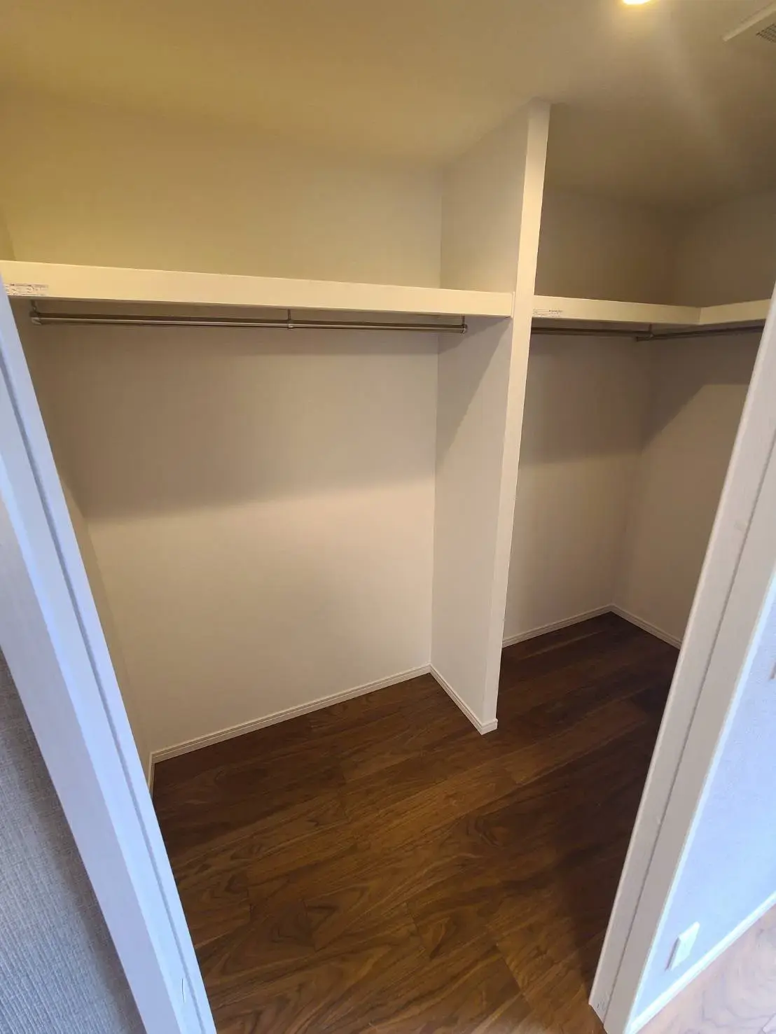 シンプルな設計のウォークインクローゼット、木製フローリング、壁に取り付けられた棚とハンガーレール