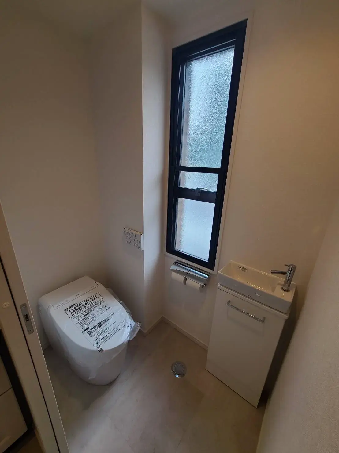 未使用のトイレと洗面台、長方形の窓とタイル張りの床が特徴のシンプルなトイレルームのインテリア