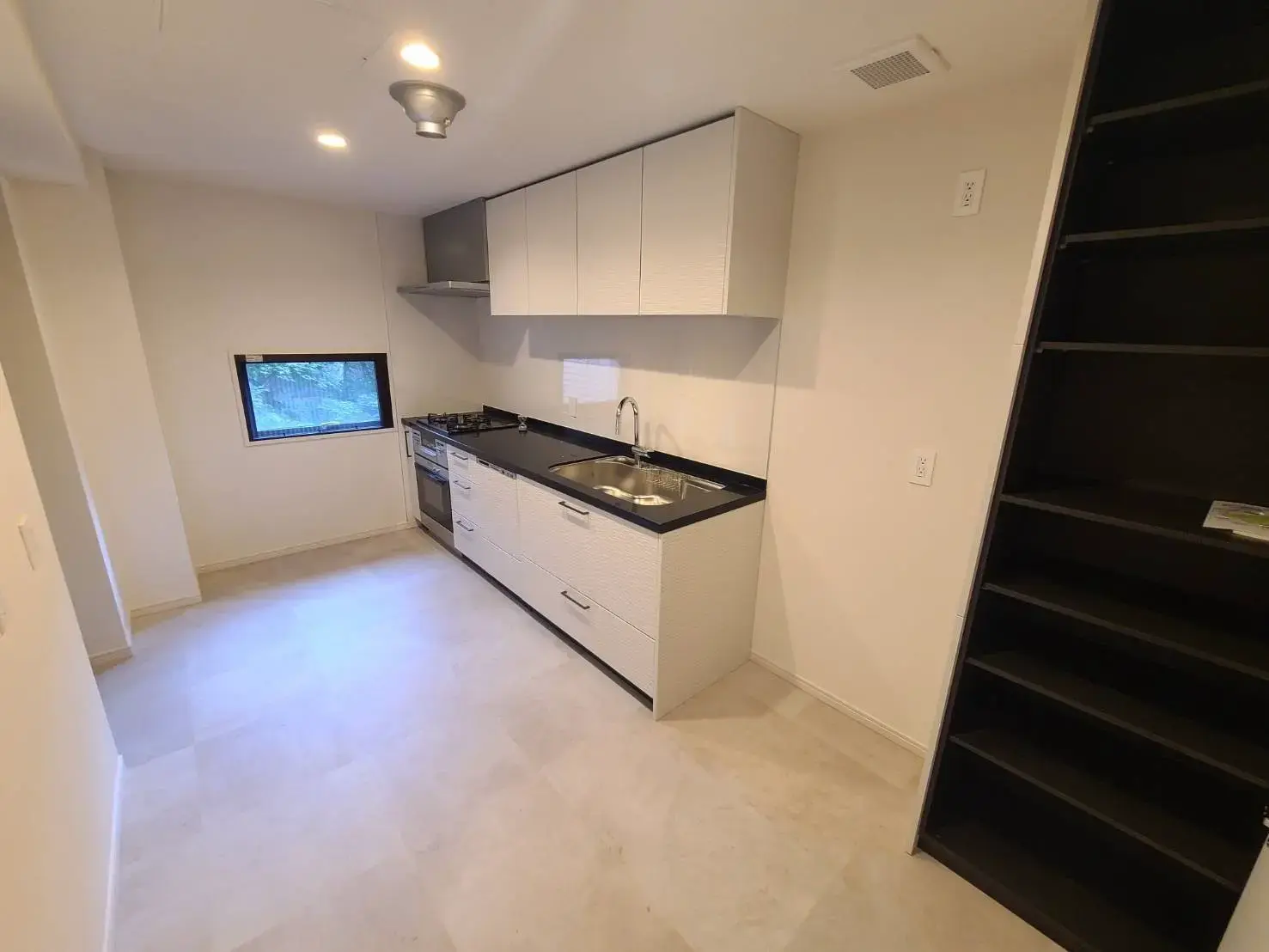 コンパクトなデザインのキッチン、白いキャビネット、黒いカウンタートップ、ガスレンジ付き、自然光が差し込む小窓