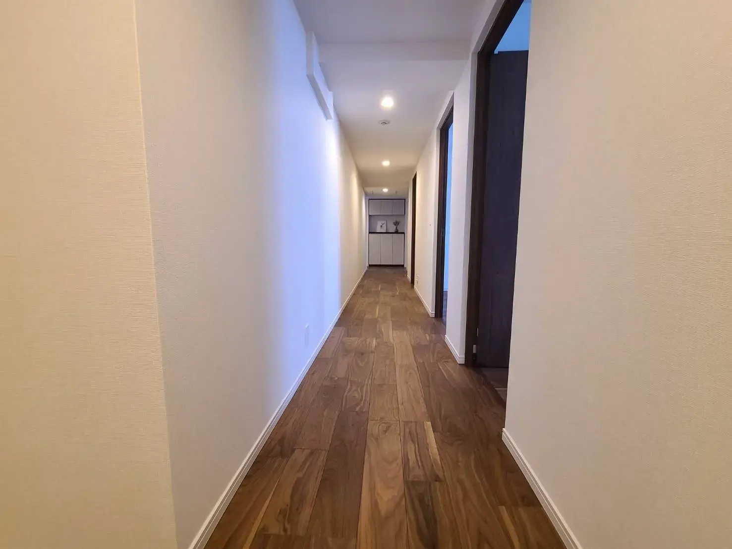 現代的な内装の廊下、木目調のフローリングと白壁、天井にダウンライトが設置された住宅インテリア