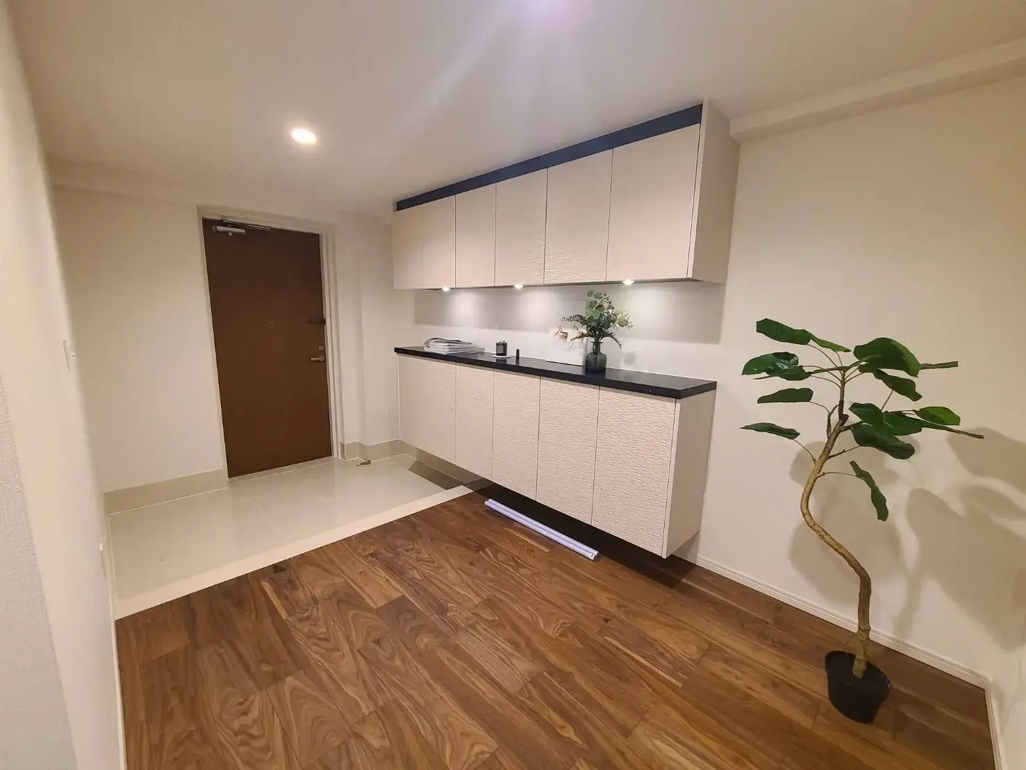 シンプルでモダンなキッチンのインテリア、白と黒のキャビネット、木目調のフローリング、植物の装飾