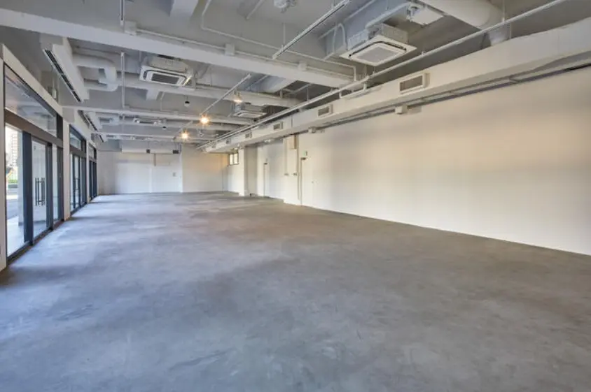 - 広々としたコンクリートの空間、白い壁と大きな窓が特徴のオープンスペース、明るい照明が設置されたインテリア