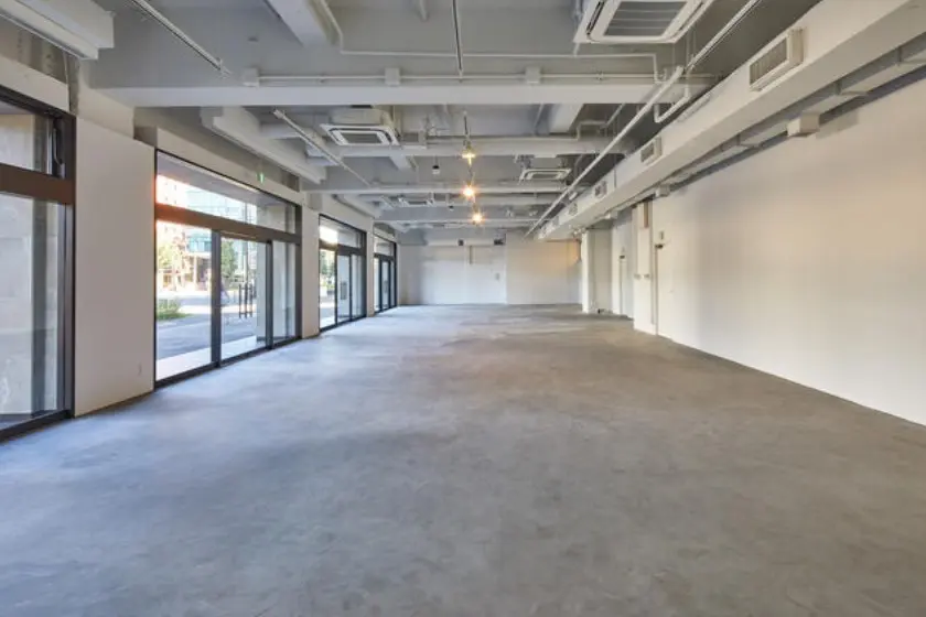 - 広々としたオープンスタイルの商業スペース、コンクリートの床と大きな窓からの自然光が特徴の内装